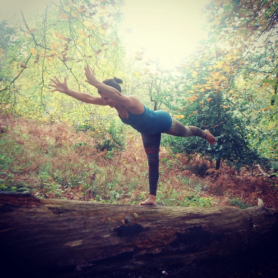 Sorayayoga practicing yoga balance pose on a fallen tree in a forest.