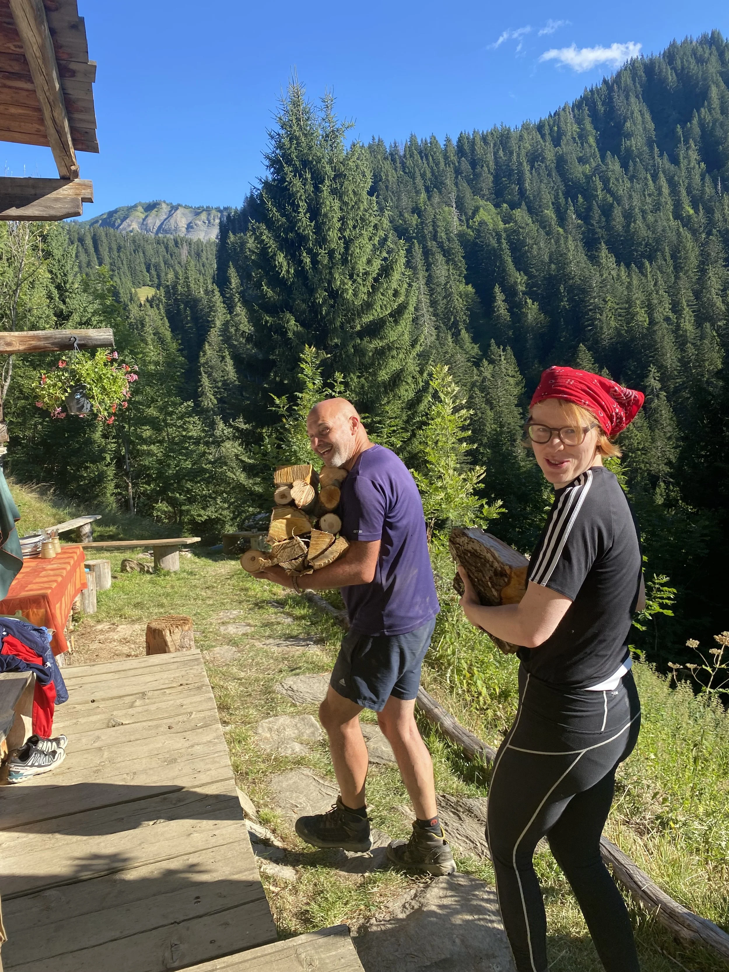 French Alps yoga retreats,  outdoors in a forested mountainous area, carrying cut firewood, smiling, 