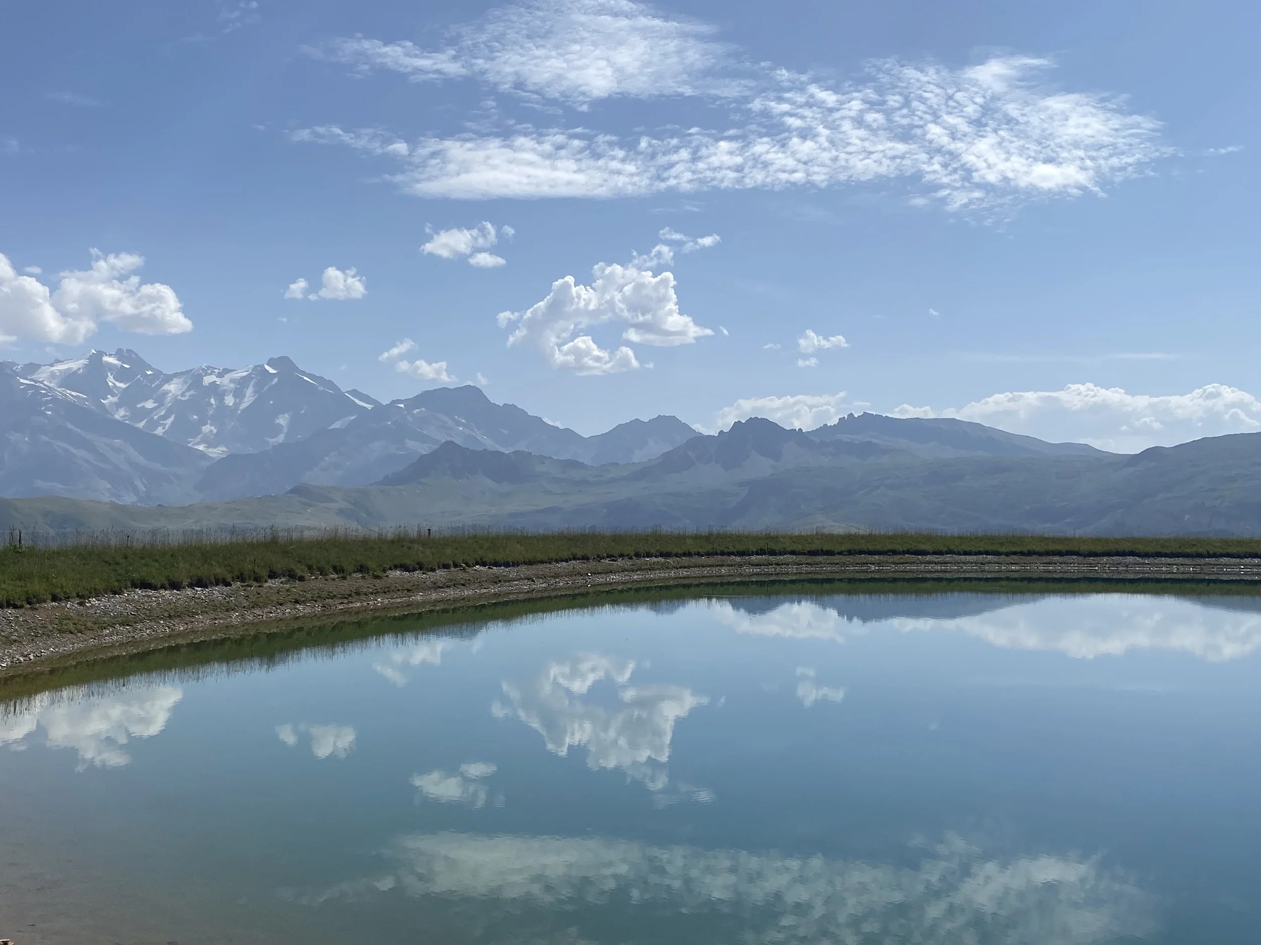 Scenic view of snow-capped mountains beneath a partly cloudy sky, with a still body of water reflecting the landscape in the foreground a blissful place for a retreat picnic