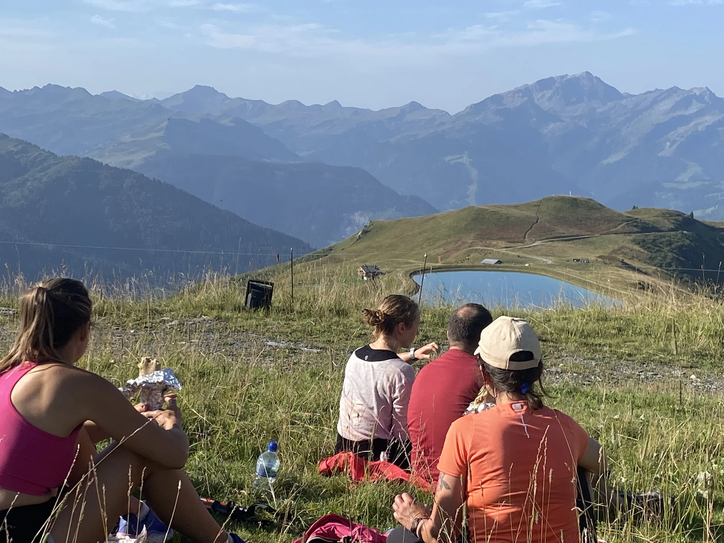 simple living mountain retreats, group picnic,  enjoying a meal with a mountain range and a small lake in the background.