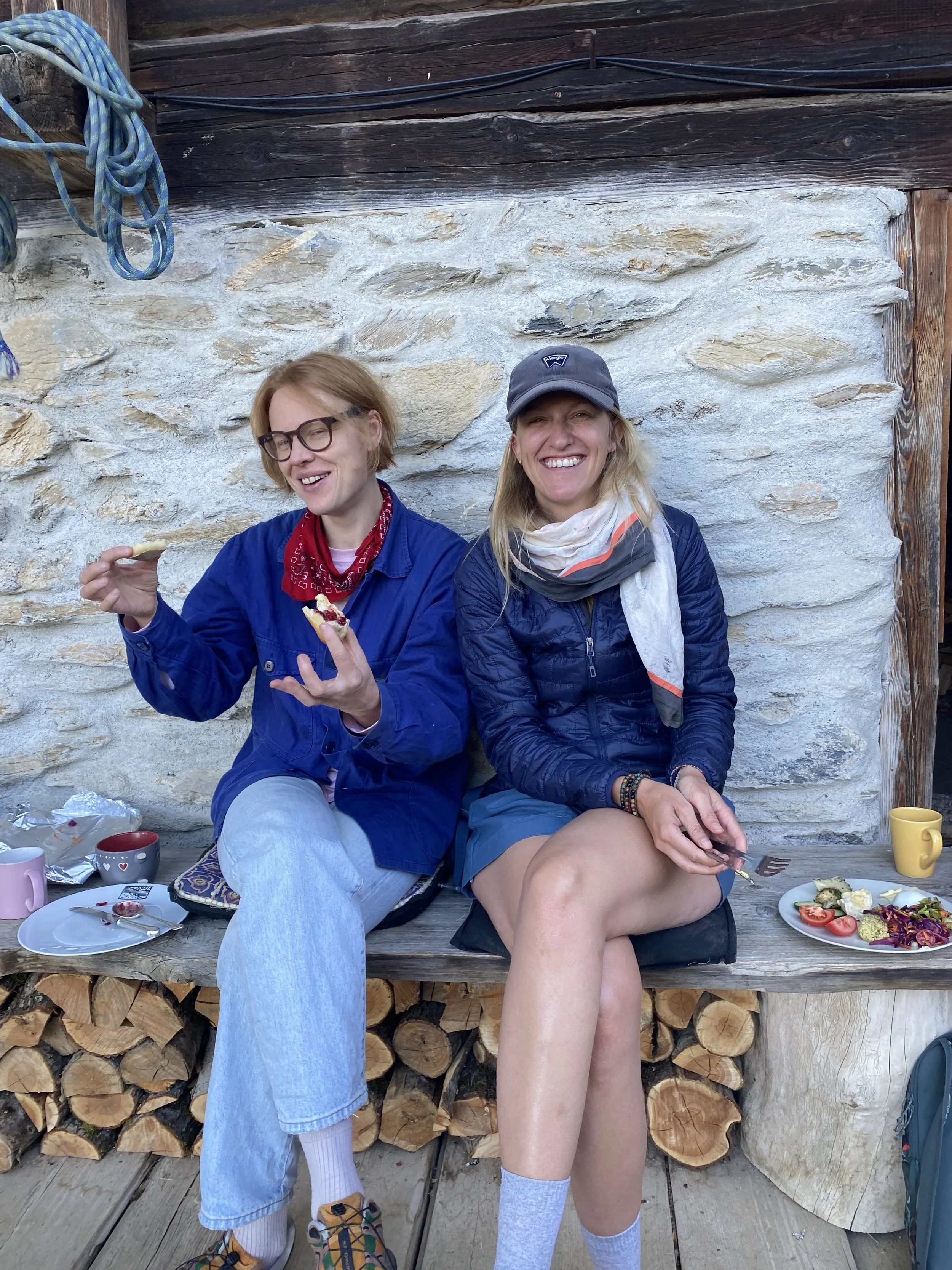 Two retreat participants sitting on a wooden bench against a stone wall, enjoying a meal.