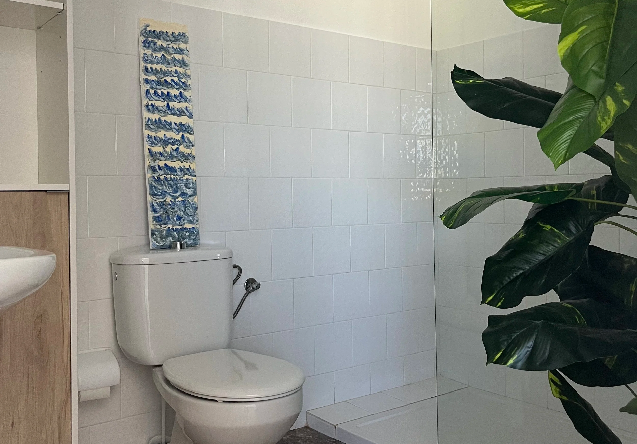 Bathroom with white toilet, partial vanity, tiled walls, glass shower enclosure, and green plant.