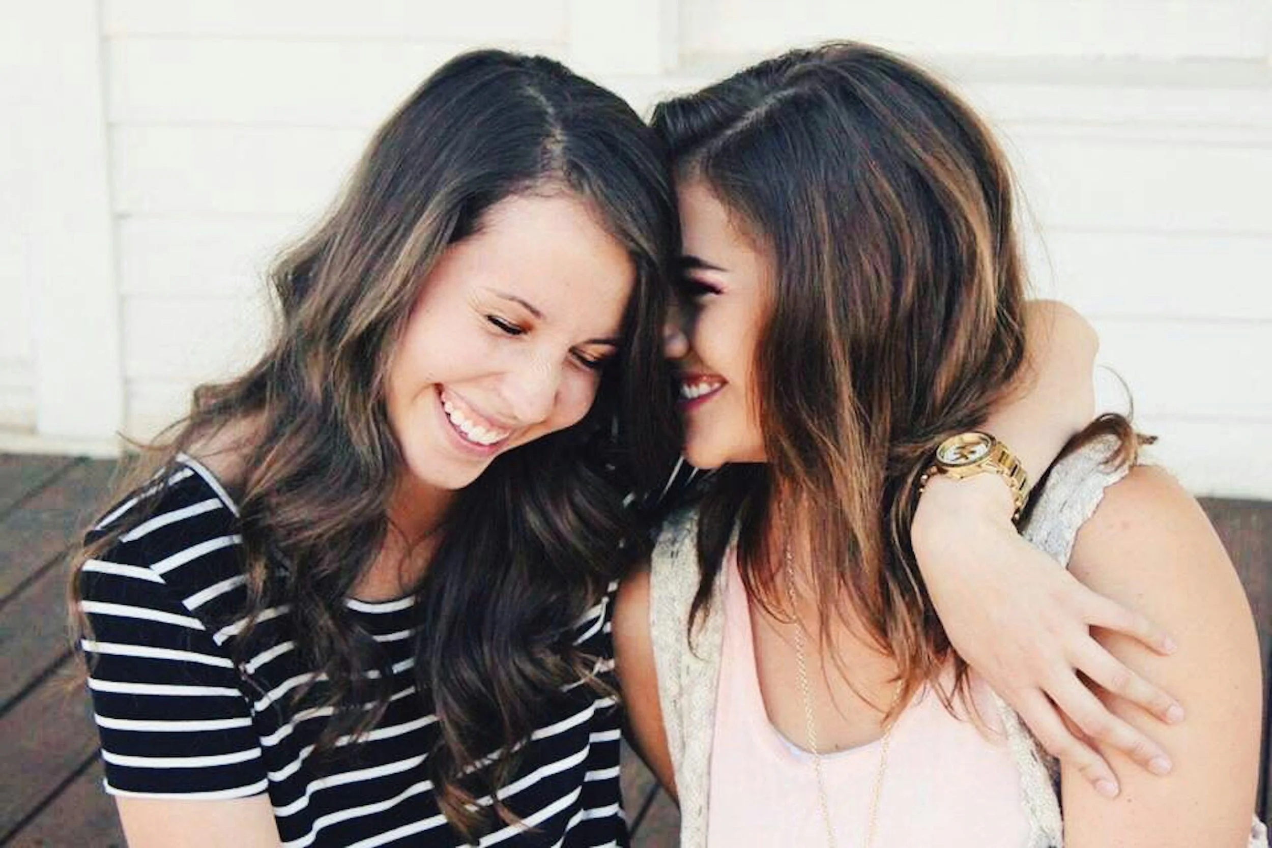 Two women are smiling and hugging each other affectionately.