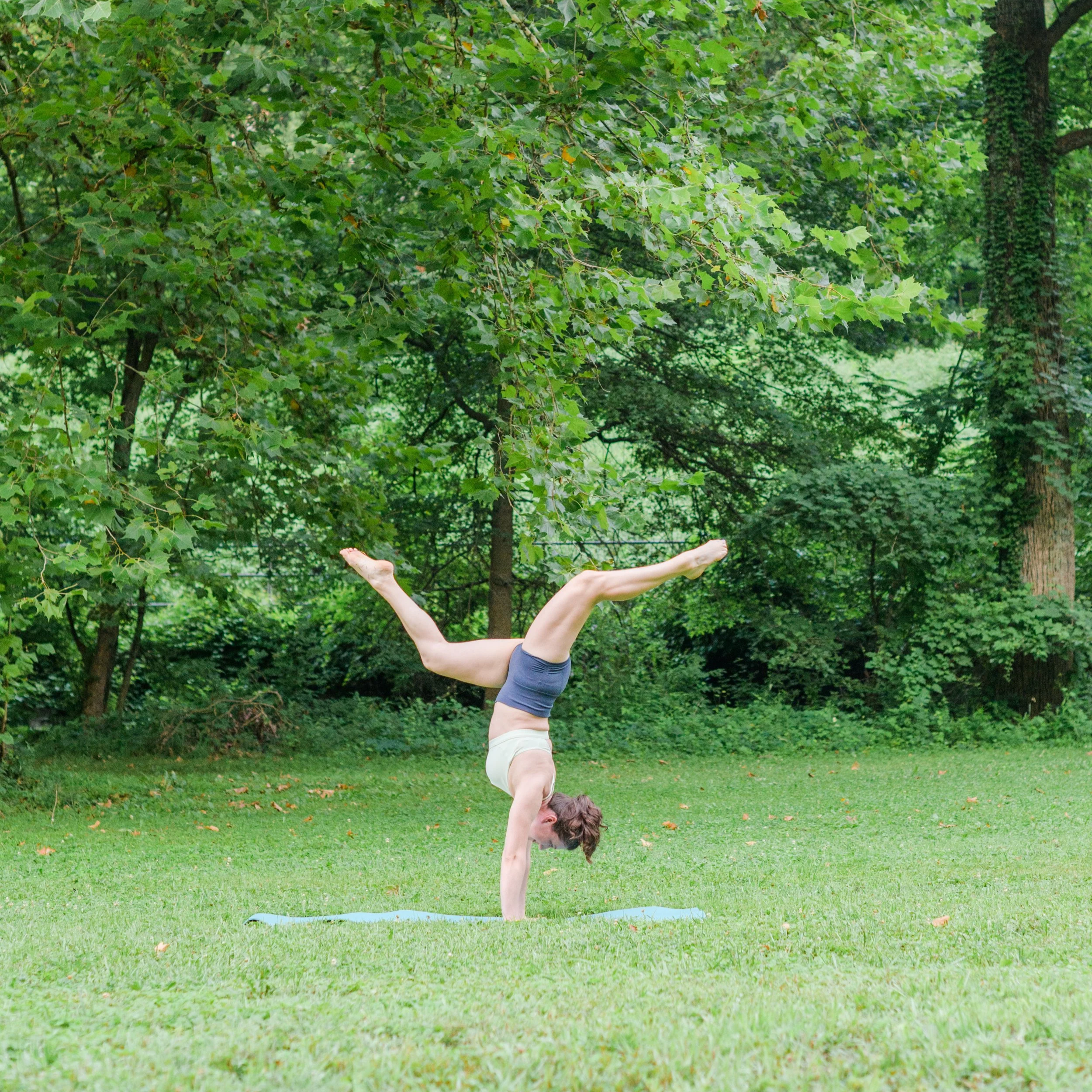 Katie LaCelle in a handstand position in a field with trees in the background