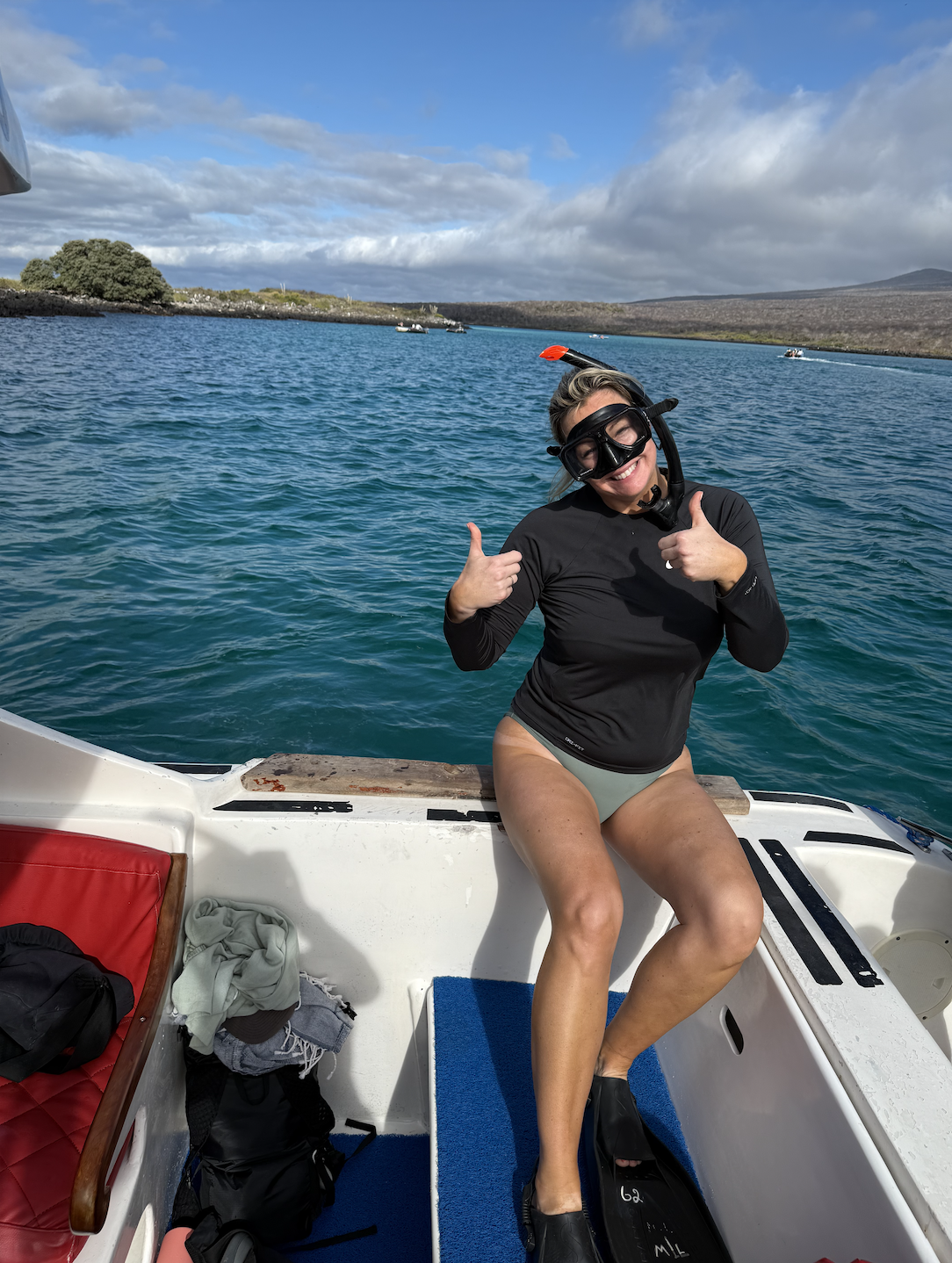Woman in snorkeling gear sitting on a boat with water, sky, and distant land in background.