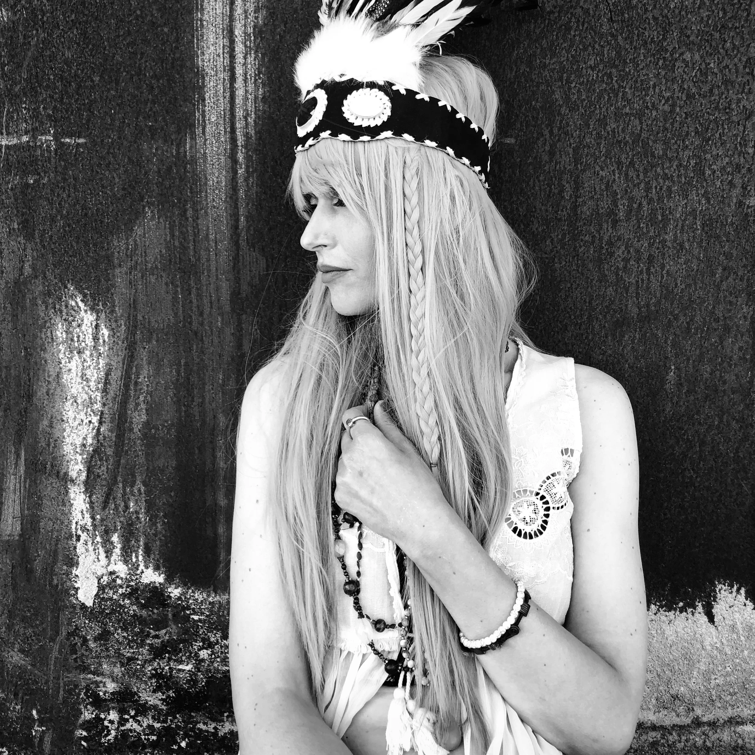 Schwarz/weiß Foto von Frau mit langen hellen Haaren, die zur Seite blickt. Dabei greift sie sich an die Halskette.