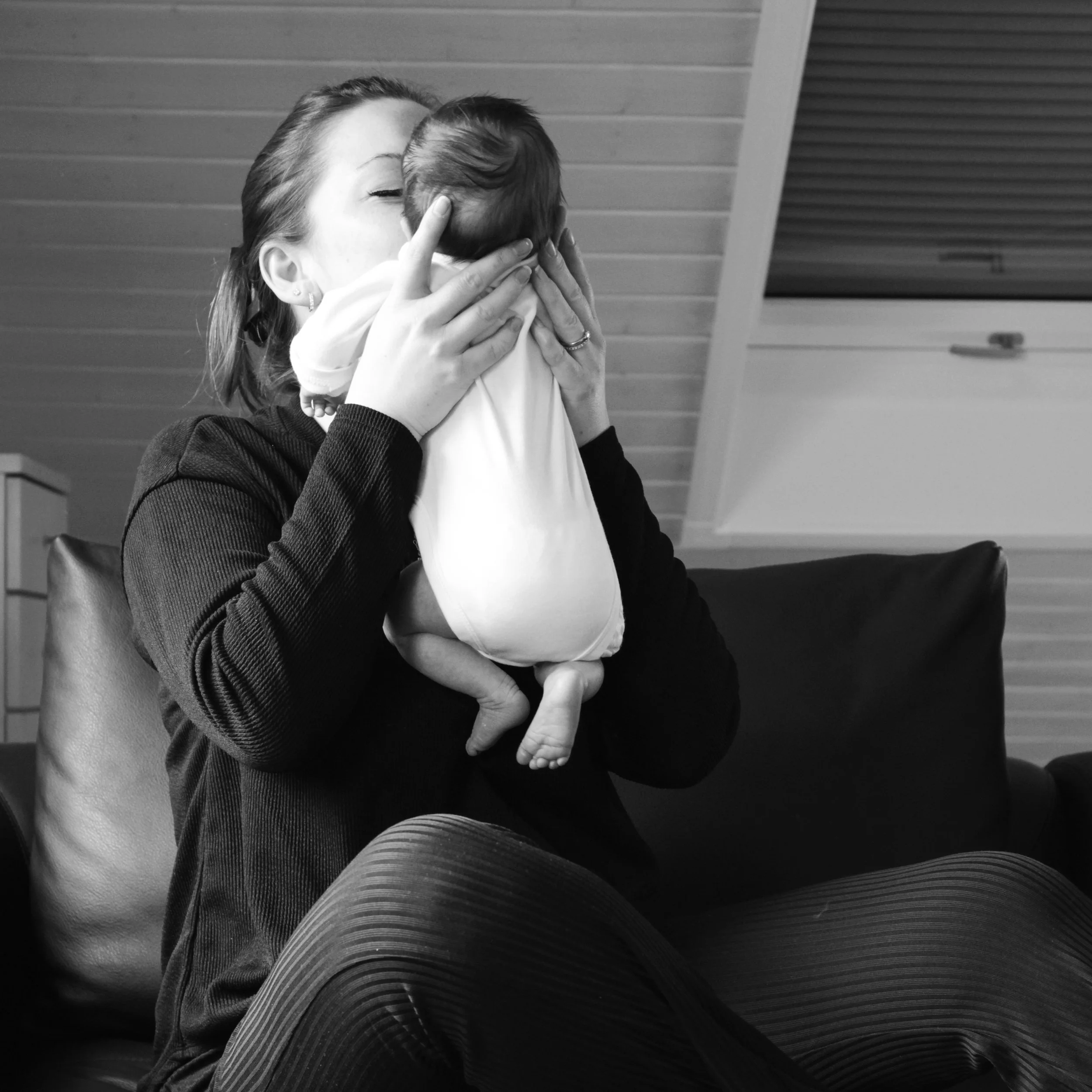 Schwarz/weiß Foto von Mutter die ihr Neugeborenes Baby hochhebt um es zu küssen.