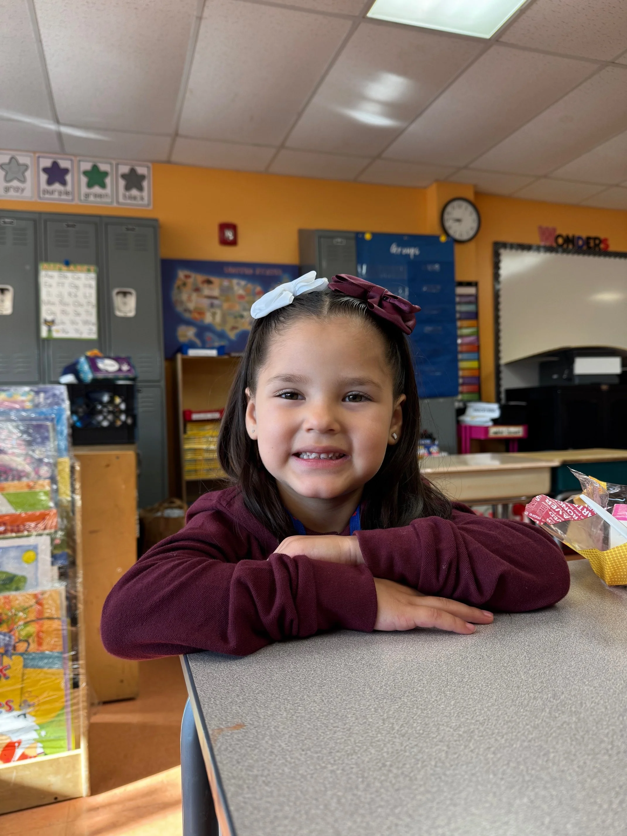 a kindergarten child sits smiling in her new classroom at challenge preparatory charter school