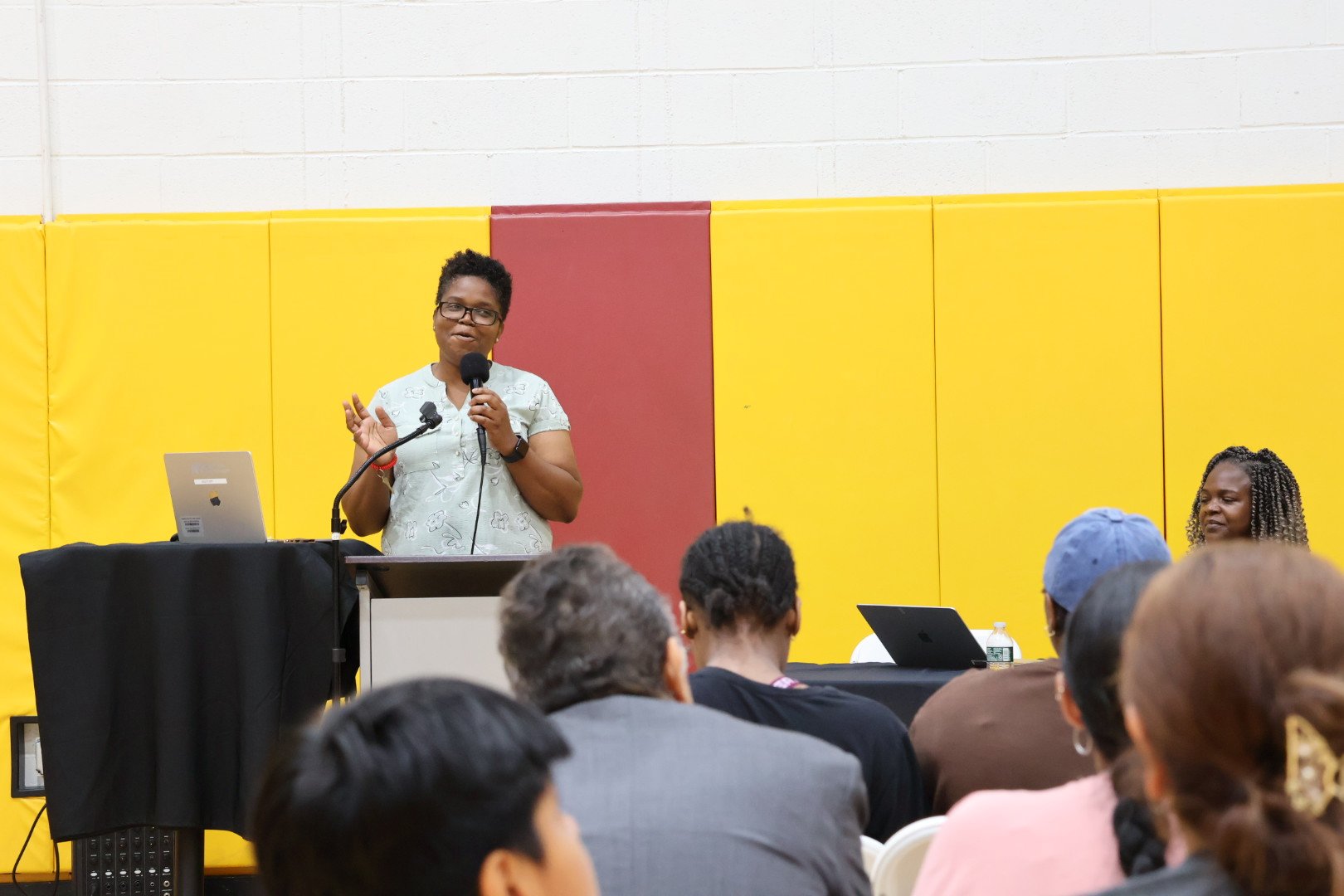 a woman stands at a podium giving a presentation while an audience sits and listens