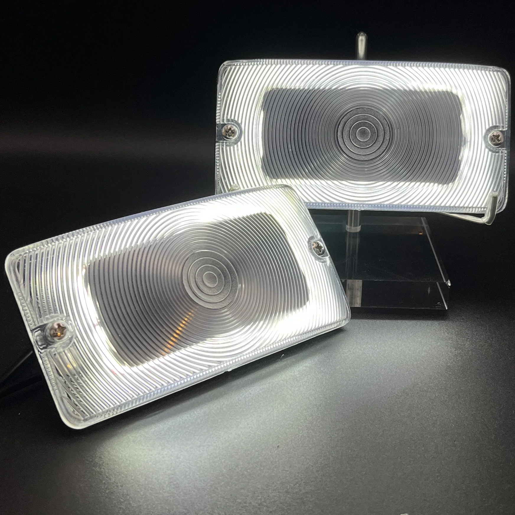 Two rectangular LED lights with concentric circle designs and clear plastic covers, mounted on stands against a black background.