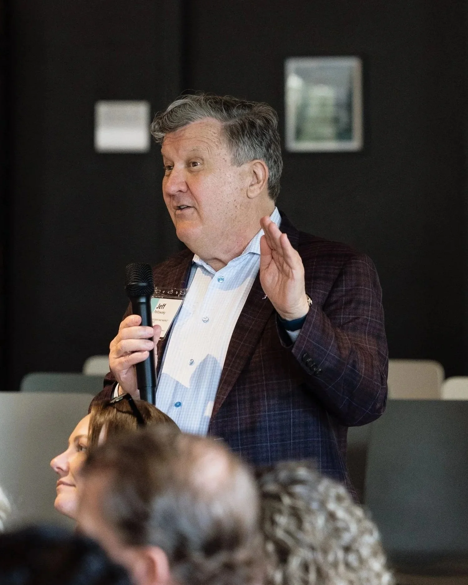 An executive in a plaid jacket speaks at the Pacific Northwest Leadership Conference, gesturing while addressing the audience indoors.