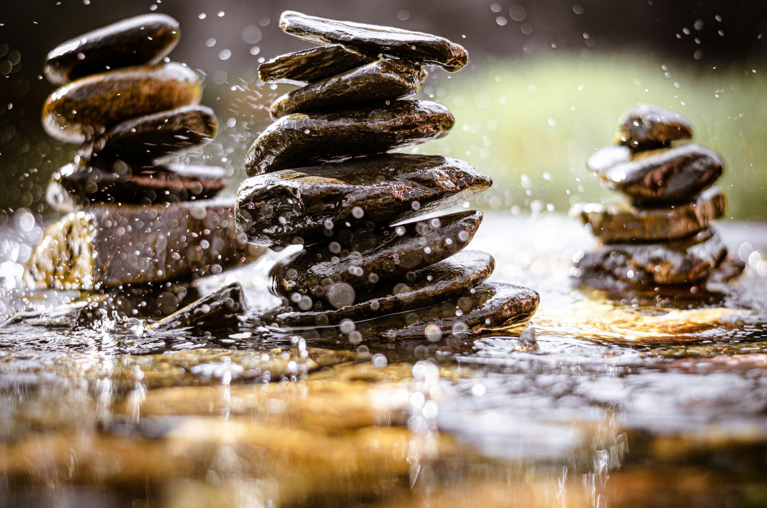 Several stacks of smooth river stones stand in a flowing stream as water splashes around them, suggesting leadership, self-awareness and the challenge of building stability in a changing environment.