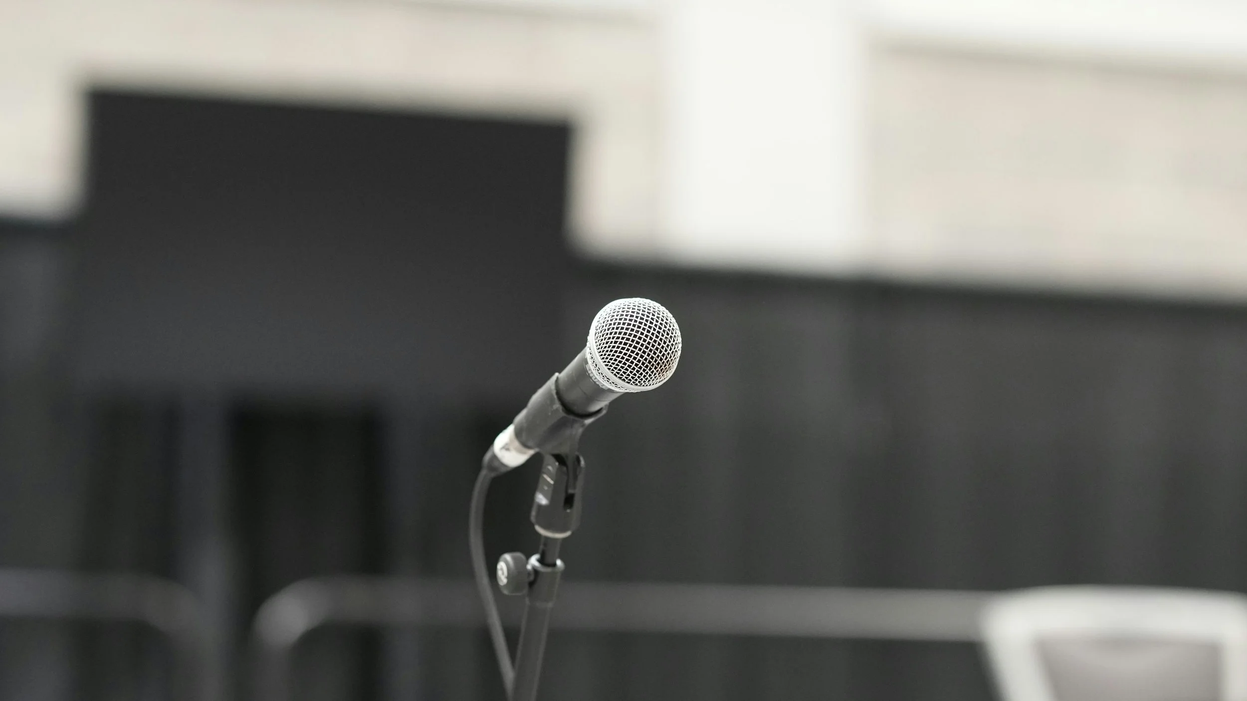 Microphone on a stand in a quiet presentation space, capturing the pause before someone speaks.