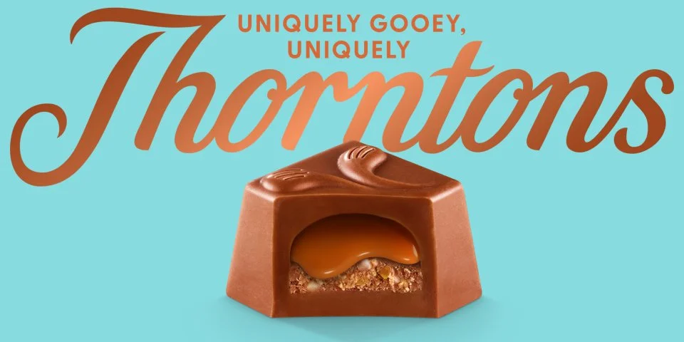 A caramel-filled chocolate candy with a smooth caramel center and crunchy base, set against a light blue background with "Uniquely Gooey, Uniquely Thorntons" written above.