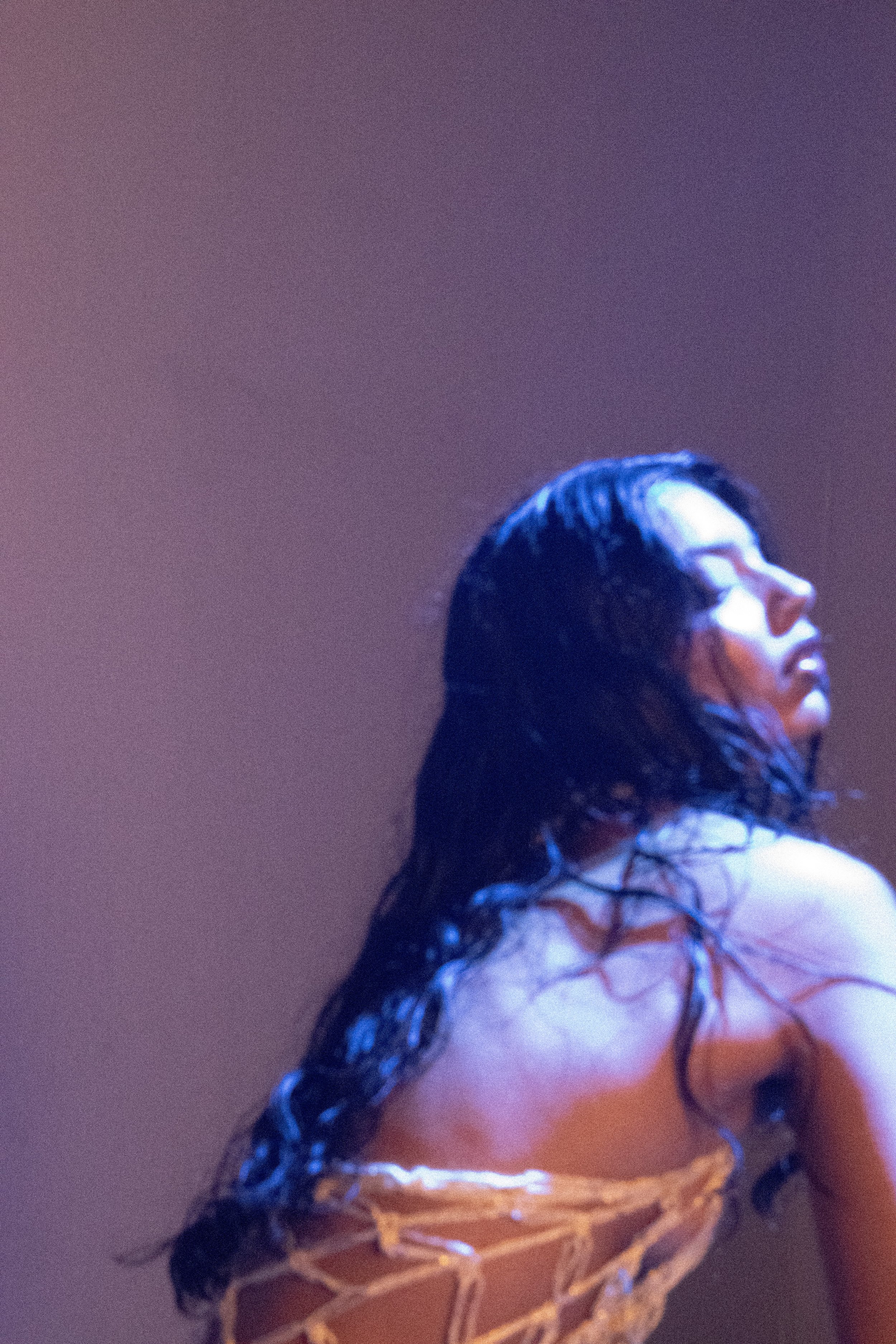 A woman with wet black hair and closed eyes poses against a plain background, in a dramatic, moody lighting photograph.