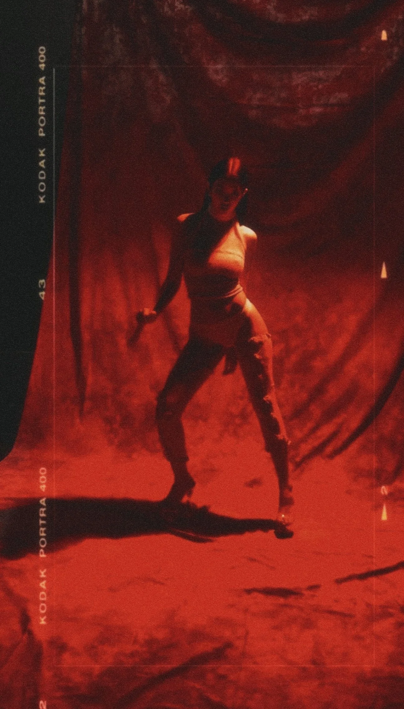 A woman in a tan top and ripped jeans posing on a red photo studio backdrop.