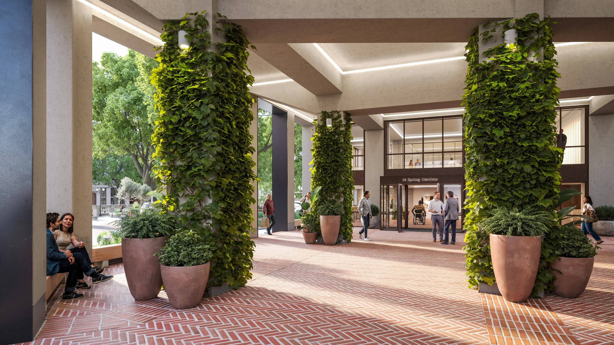 Modern building entrance with large potted plants, green vines on columns, and people walking and sitting outside on a sunny day.