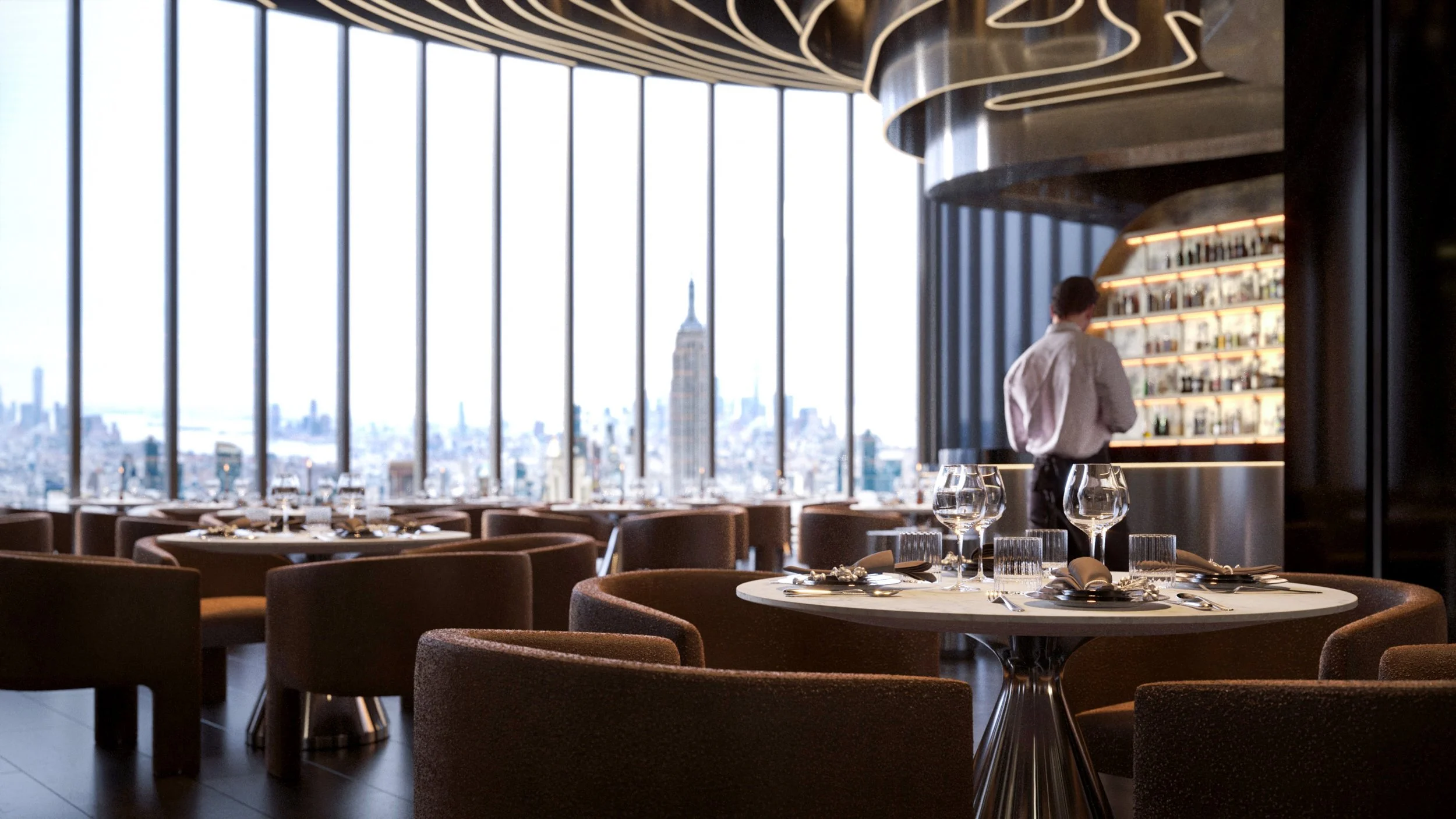 Elegant restaurant interior with large windows offering city skyline views, including the Empire State Building, with tables set with wine glasses and napkins, and a bartender behind a lit bar.