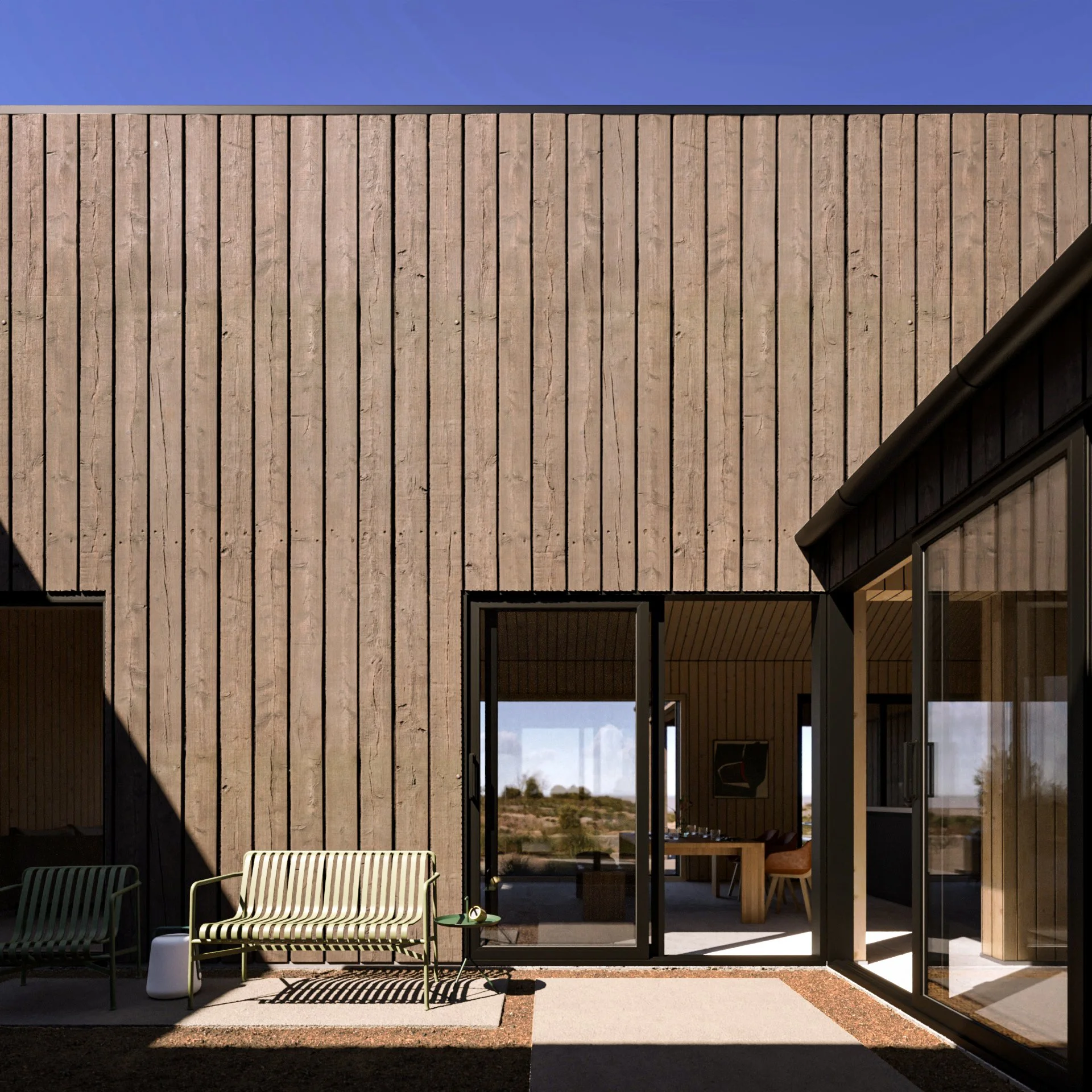 View of a modern building with vertical wooden siding, glass doors, and outdoor seating; clear blue sky in the background.