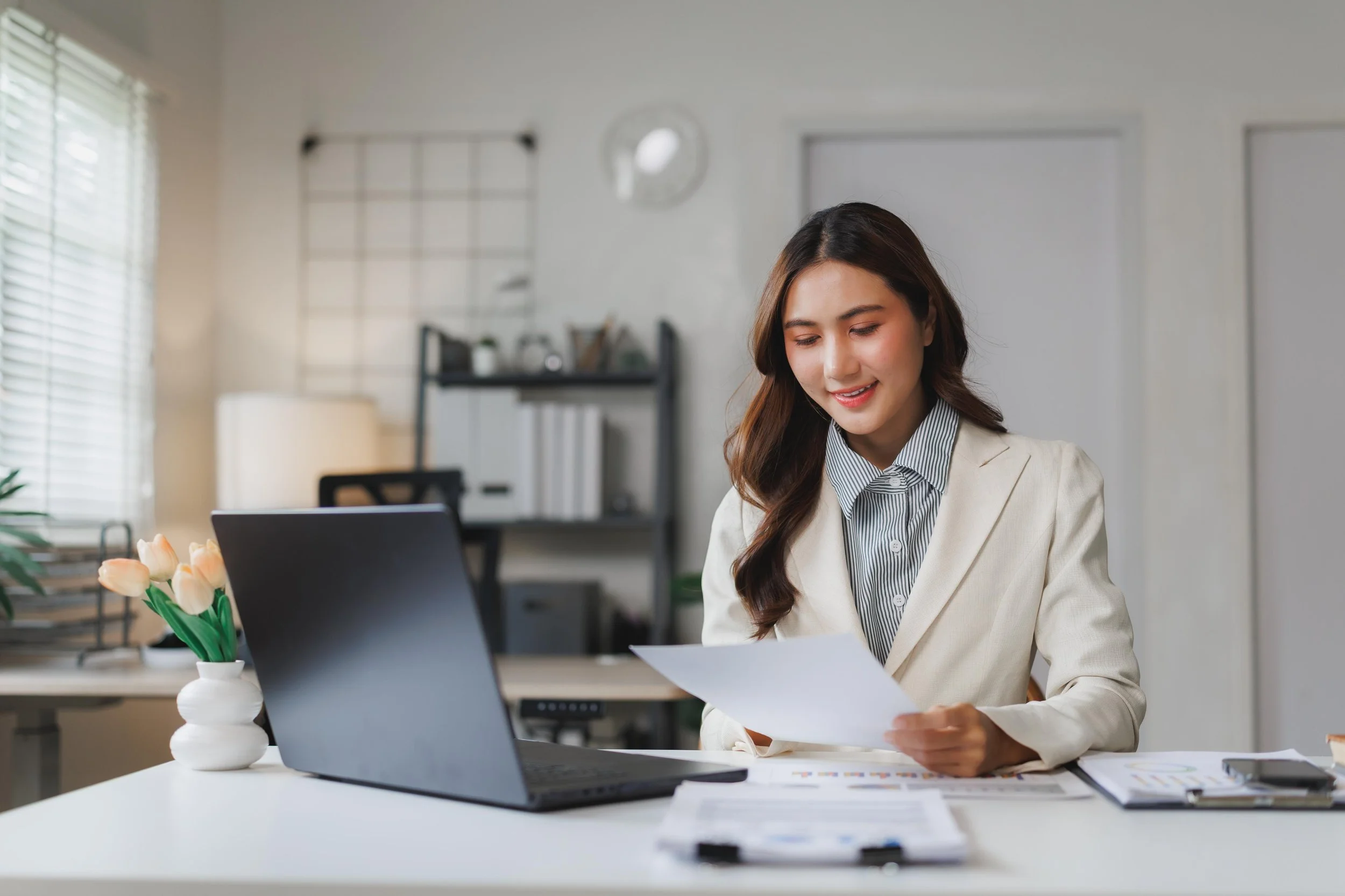 Filipino administrative professional reviewing documents while working at a computer.