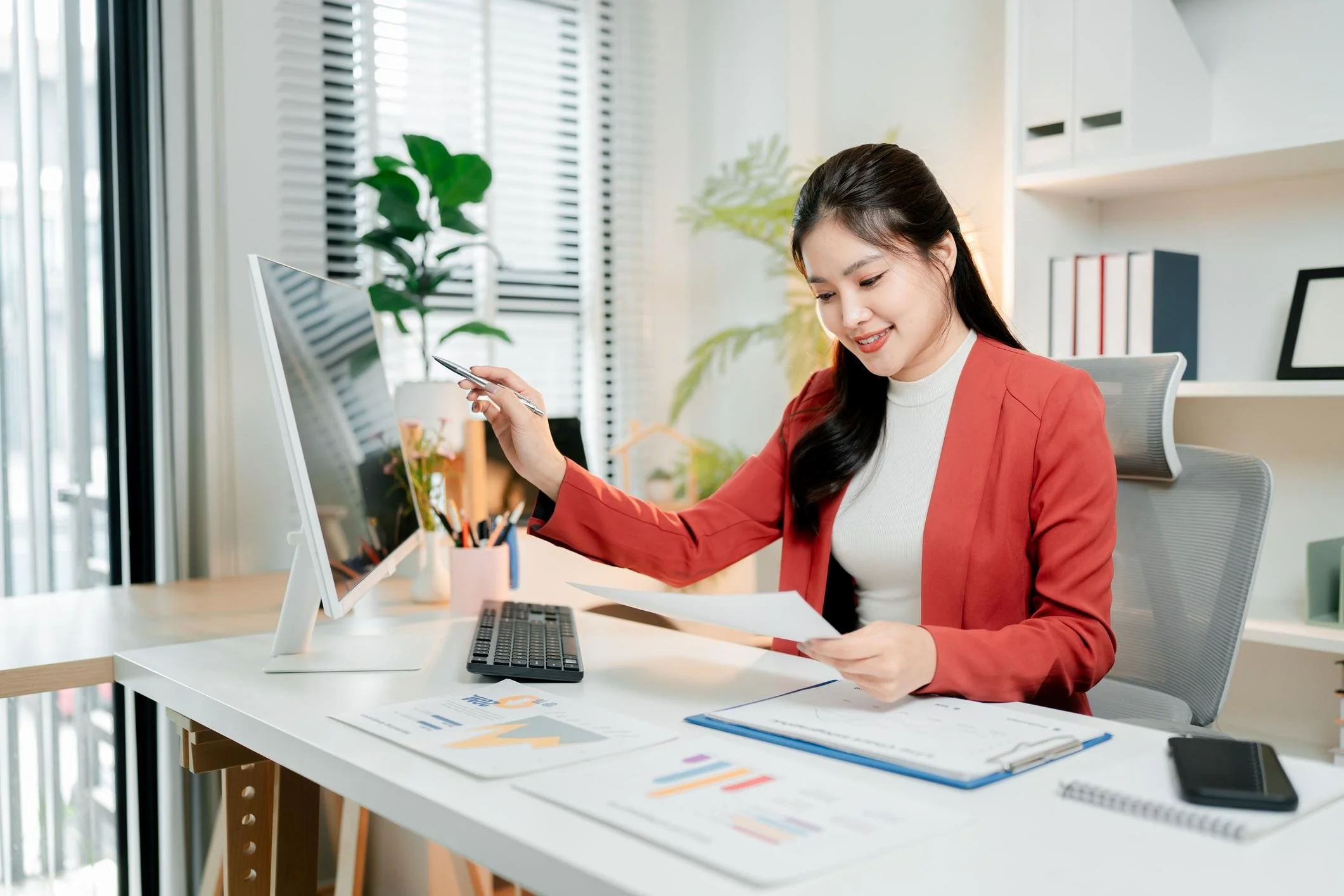 Filipino administrative professional reviewing documents while working at a computer.
