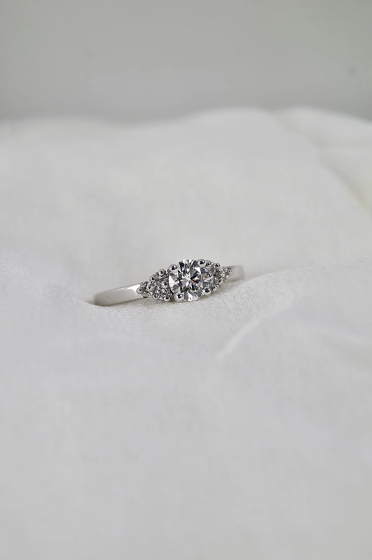 Bague en argent avec une pierre centrale ronde entourée de petites pierres, posée sur une surface en tissu blanc.