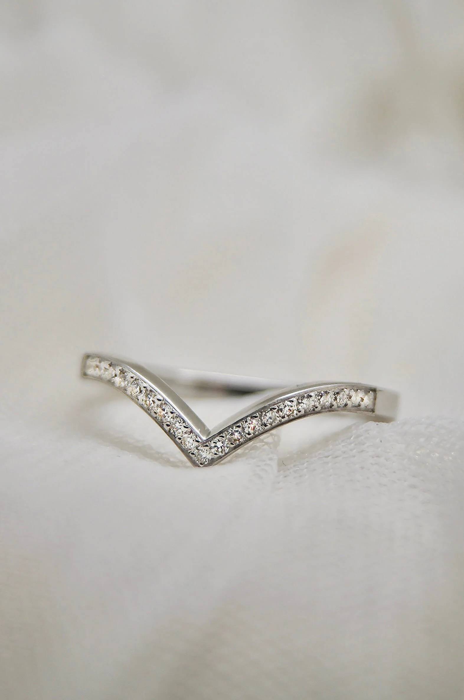 Bague en argent avec des diamants incrustés, disposée en forme de V sur une mousseline blanche.