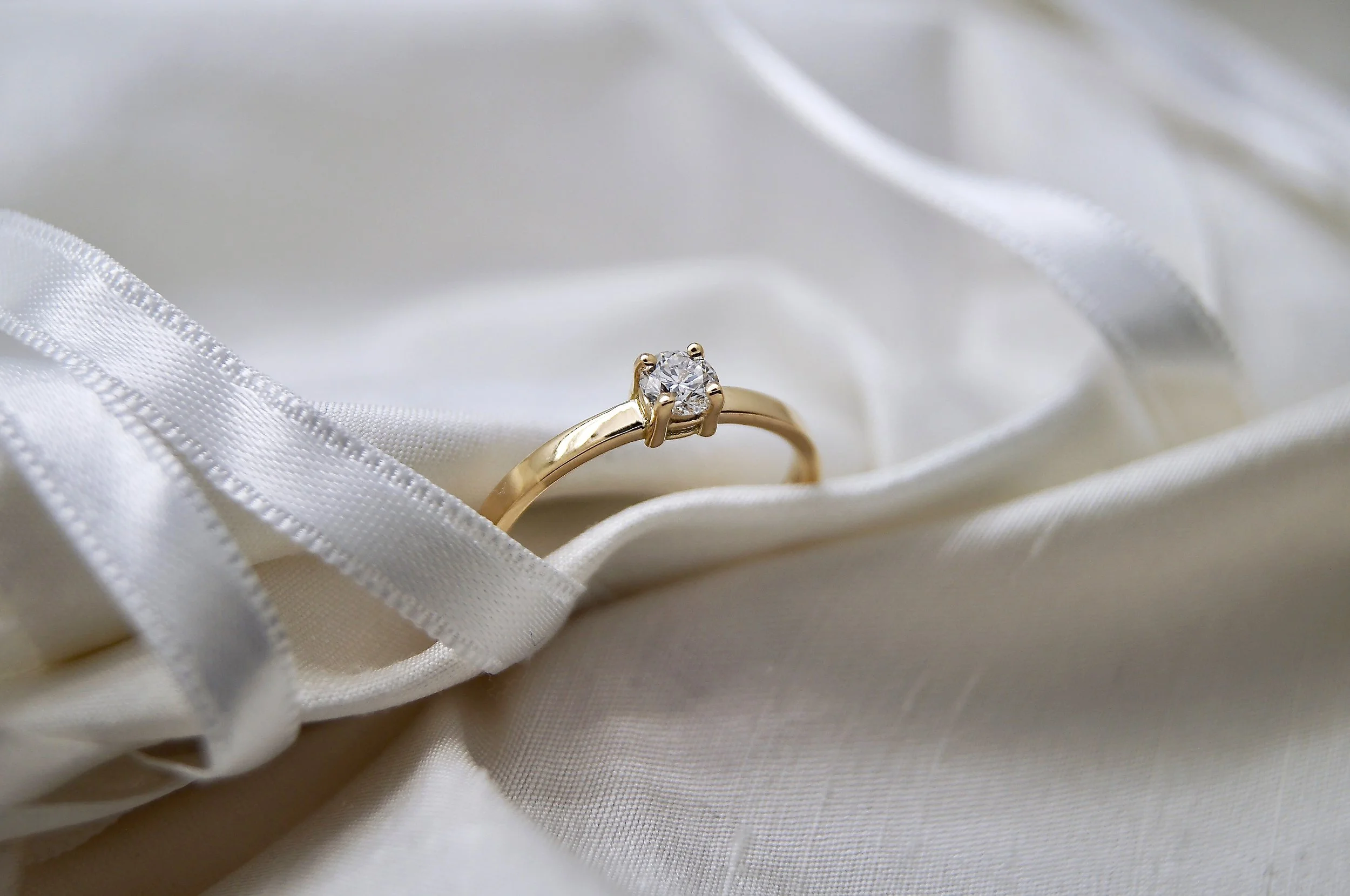 Une solitaire en or jaune avec un diamant est posée sur un tissu blanc en satin, entourée d'une bande de satin.