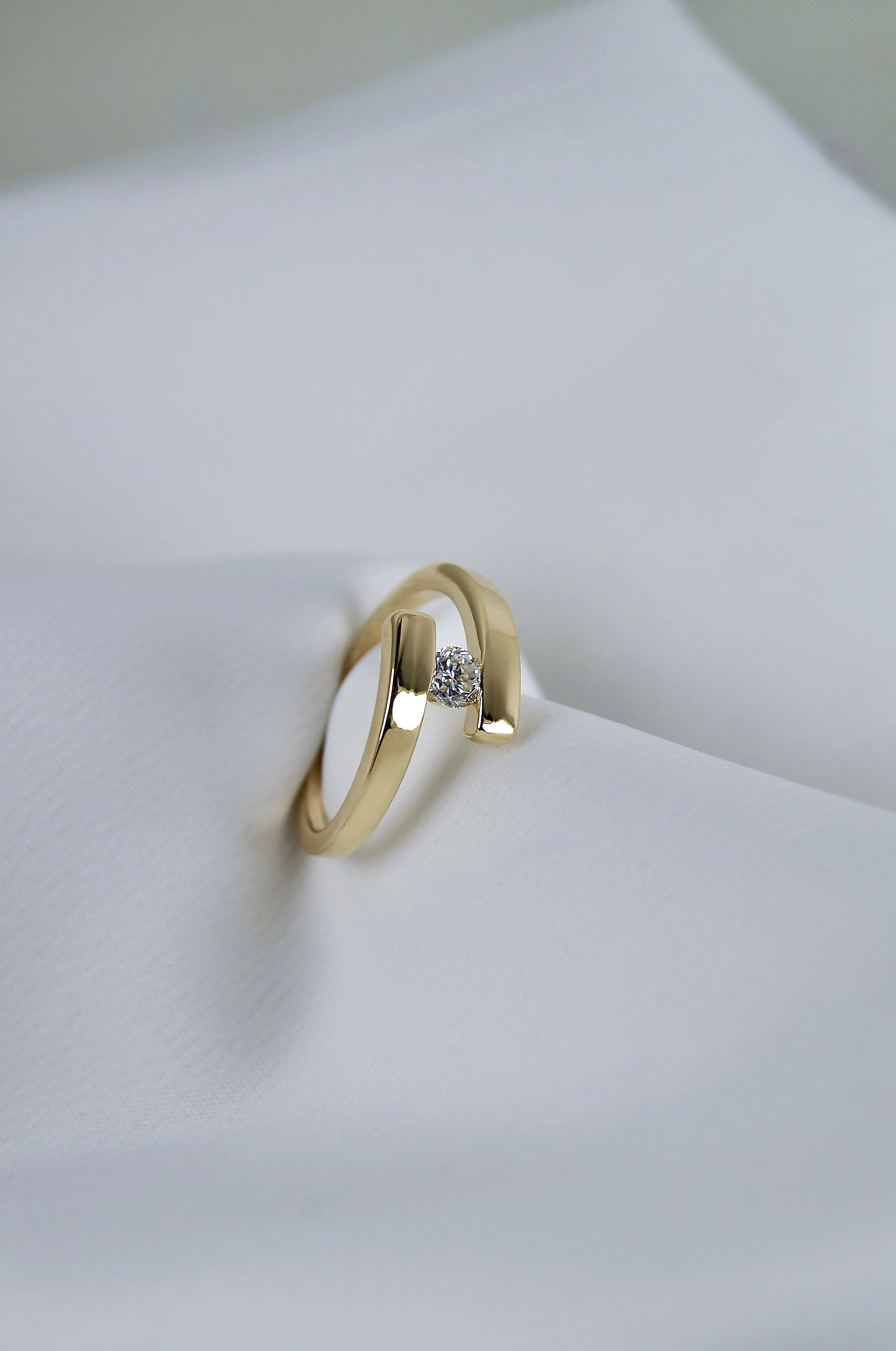 Une bague en or avec un diamant, posée sur un fond blanc élégant.