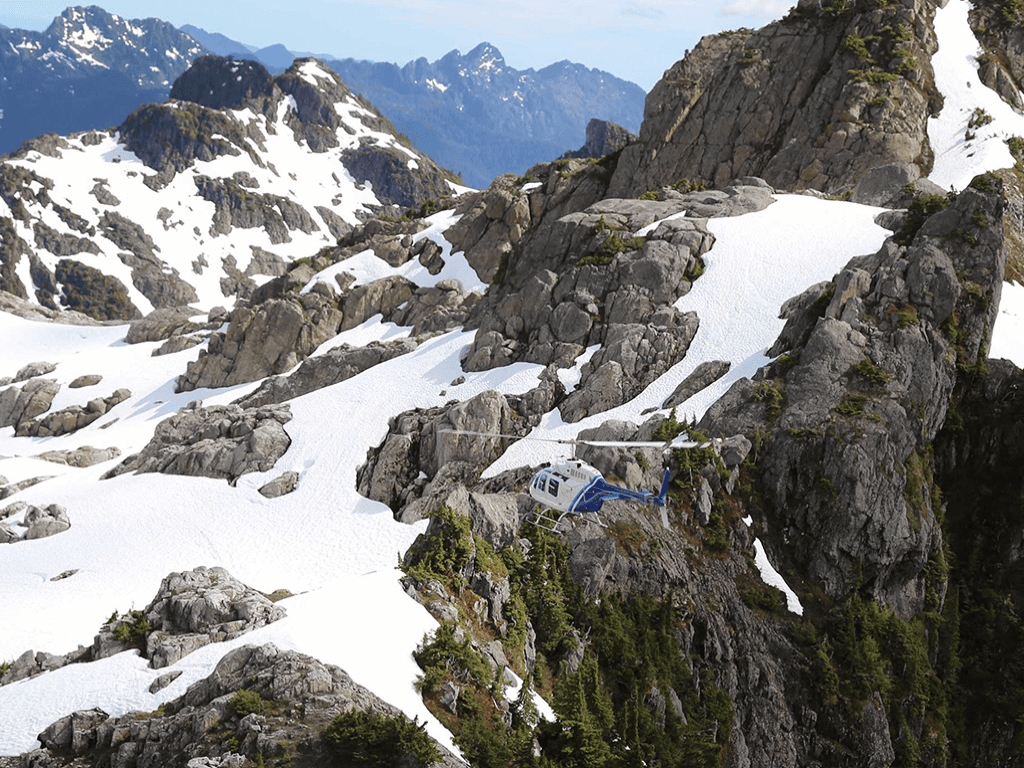 Helicopter flying over snow-covered mountains in British Columbia, symbolizing remote wilderness experiences beyond Vancouver.