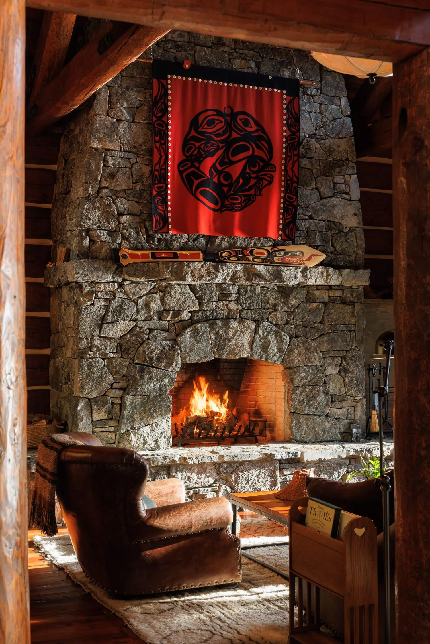 The interior lounge of Fawn Bluff Private Lodge featuring a stone fireplace and Indigenous artwork, highlighting the destination's connection to the Homalco First Nation.