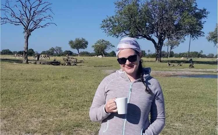 Safari travel advisor Karen Tatum enjoying morning coffee on safari with zebras grazing in the background.