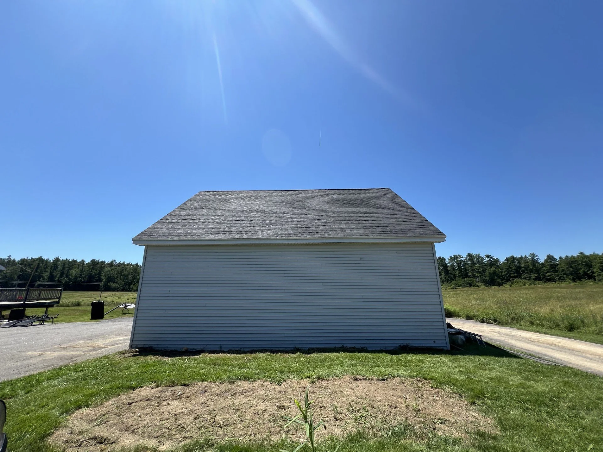 Rear view of a white building with a gray shingle roof under a clear blue sky, with a grassy area and open field surrounding it.