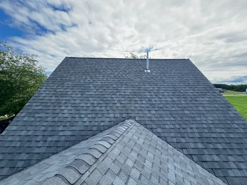 Close view of asphalt shingle courses, ridge caps and a roof pipe.