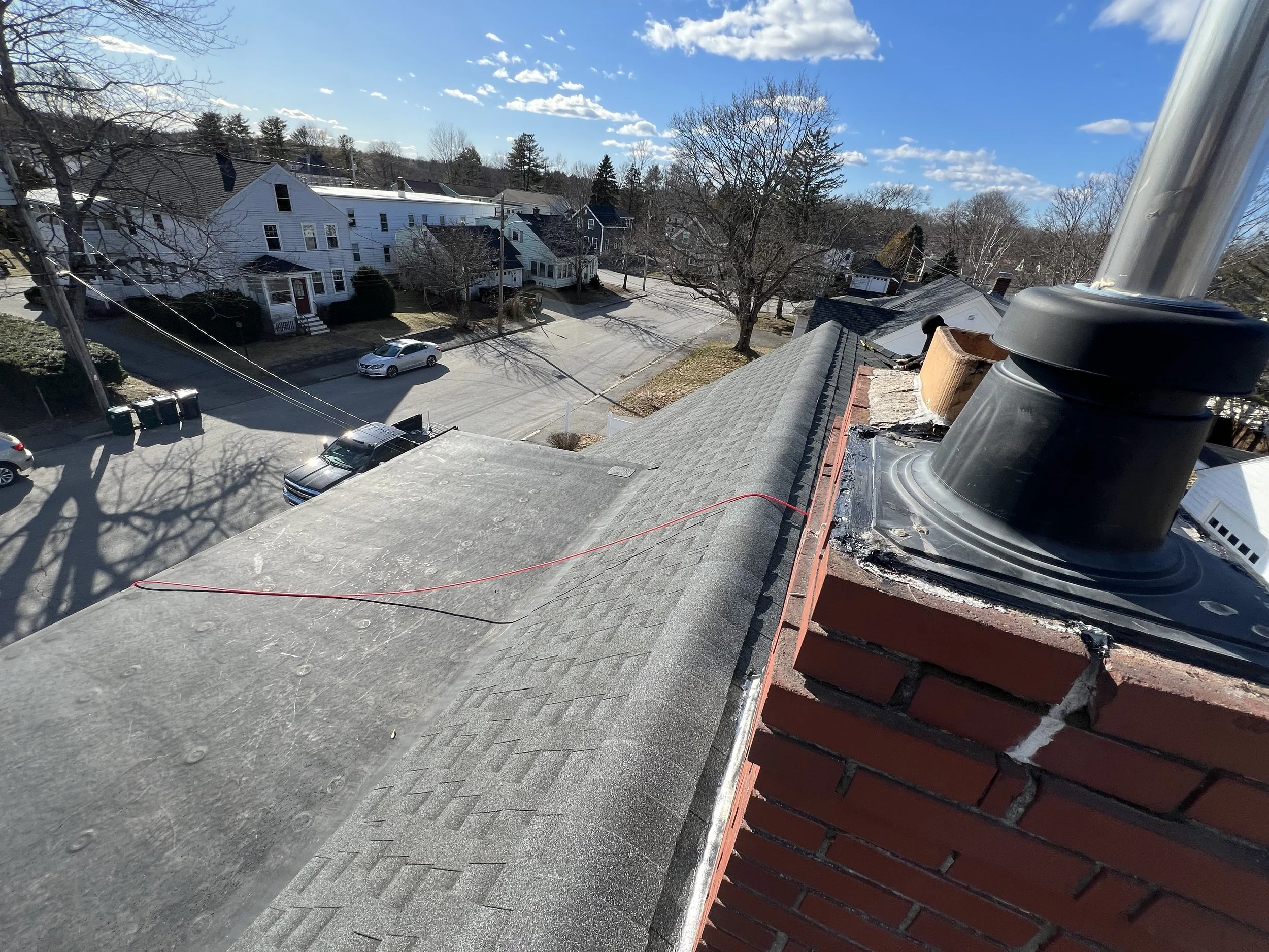 View from a rooftop showing neighboring houses, street, trees, and parked cars on a sunny day
