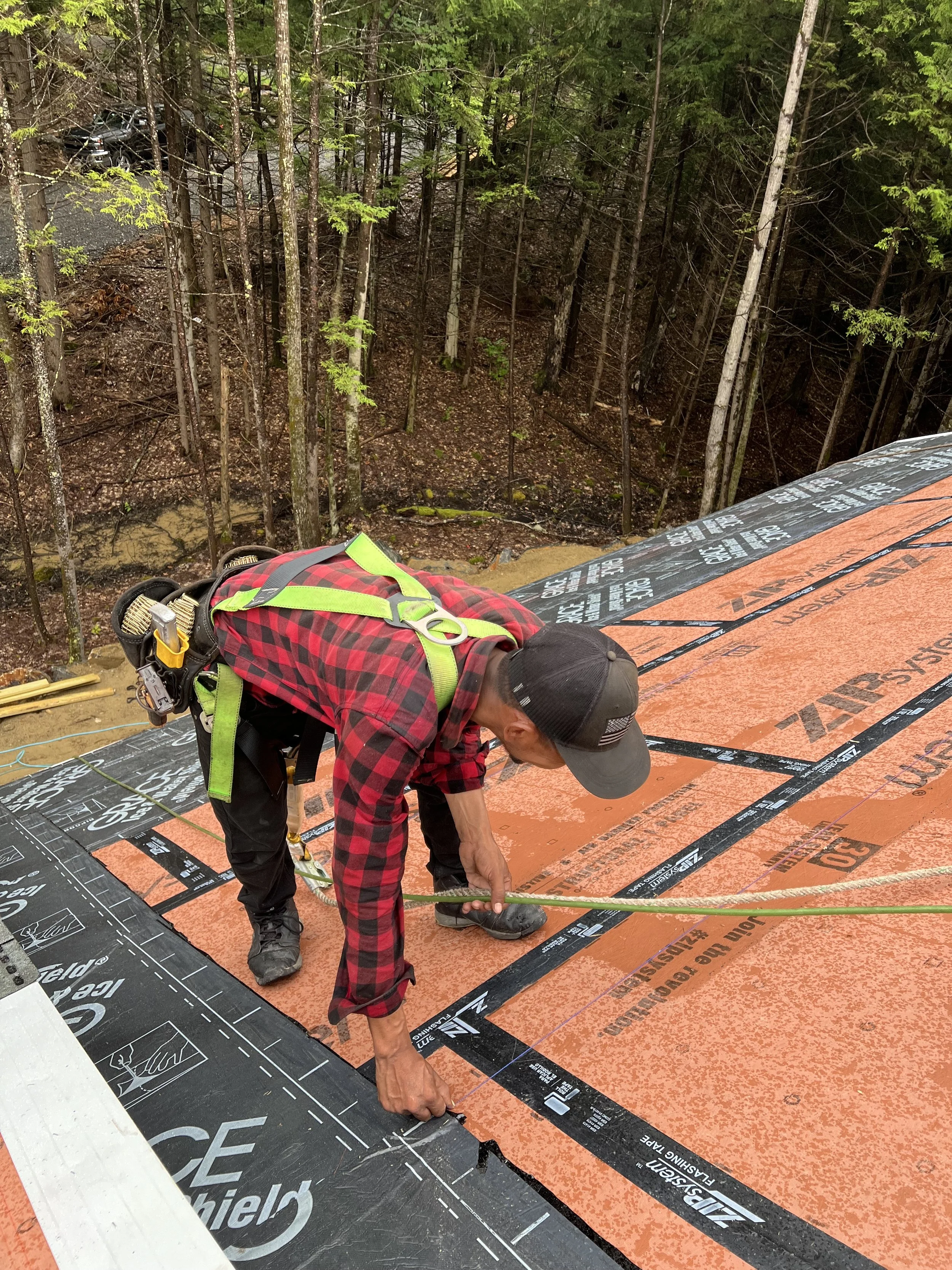 Construction worker installing roof underlayment on a building with a forested background.