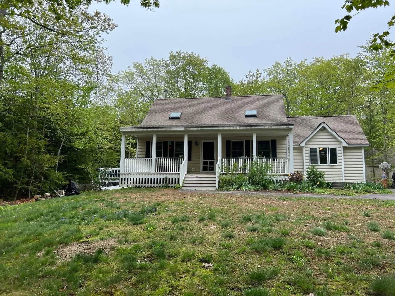 A house with a front porch and stairs, surrounded by a grassy yard with some plants, and trees in the background.