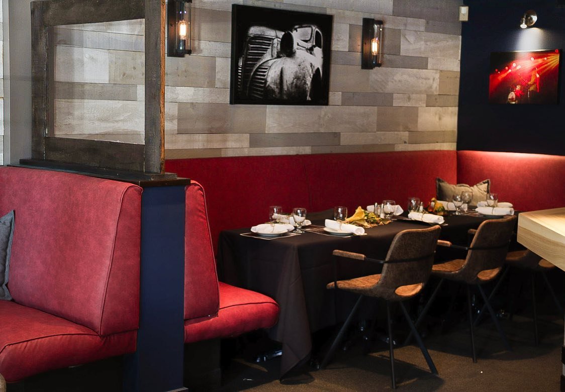 Interior of a restaurant with red booth seating, a black-clothed table set for dining, and art on the walls.