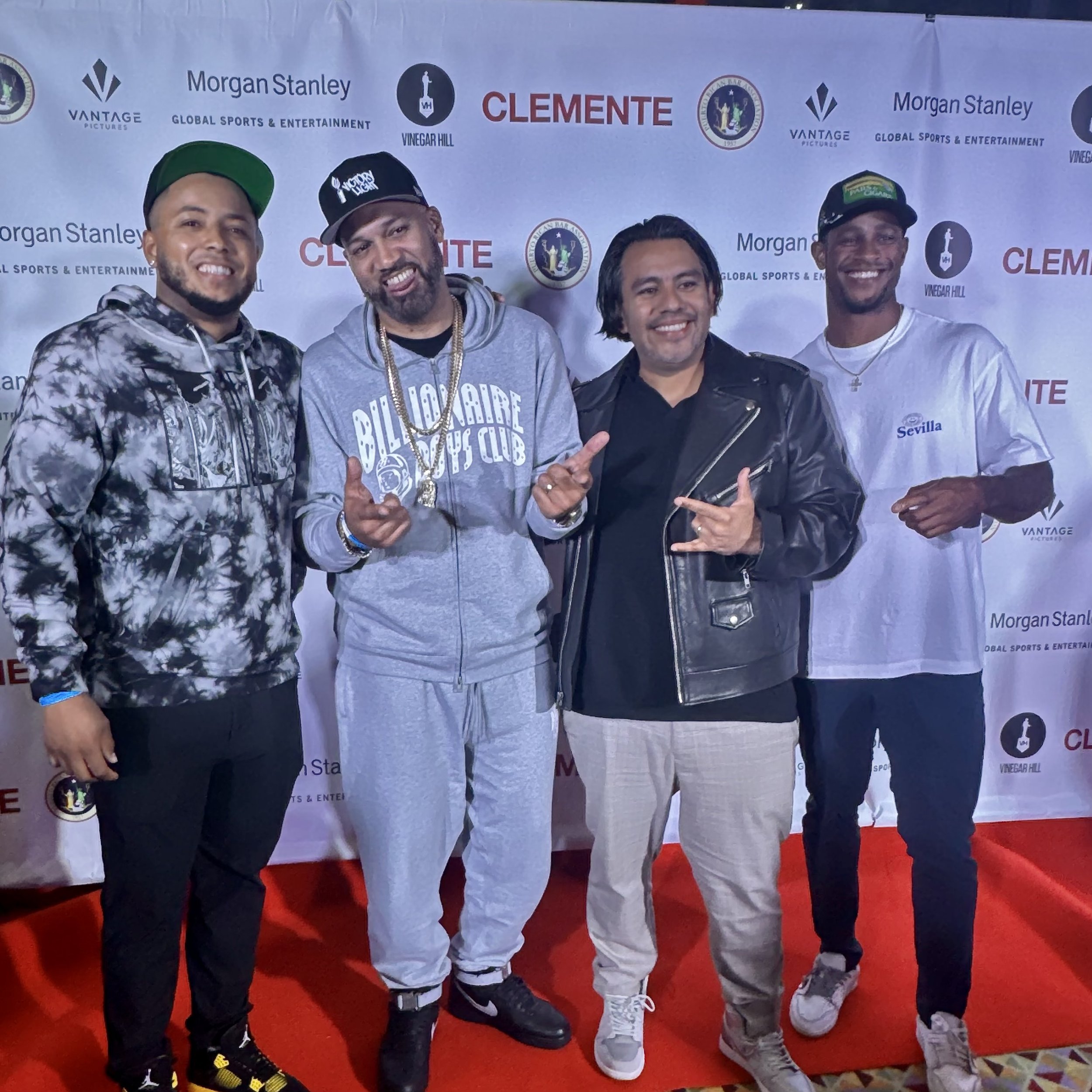 Four men standing in front of a branded backdrop at an event, smiling and posing for the photo.