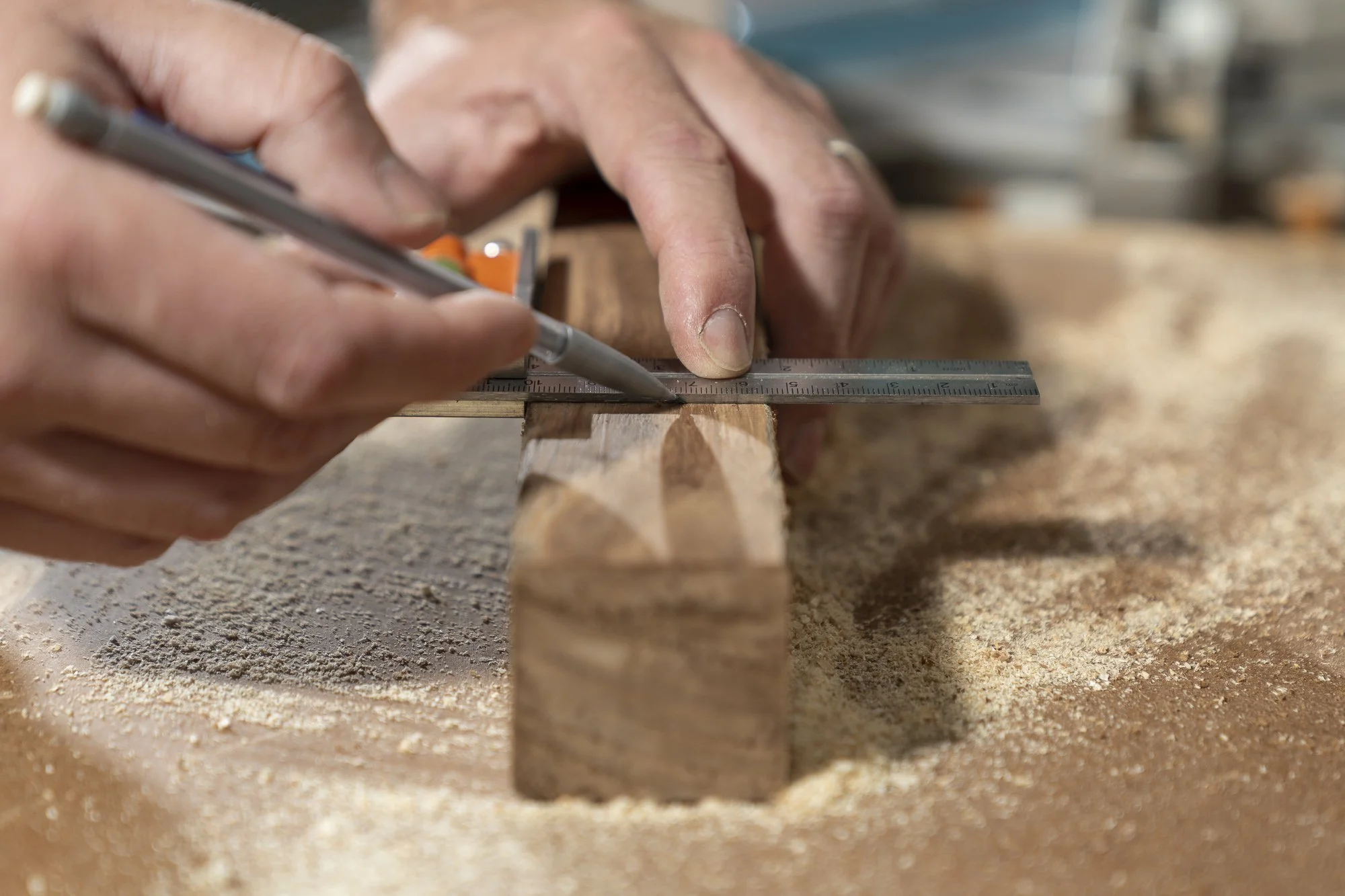 The Freshfield Woodsmith: Close-up of a person's hands using a ruler and protractor to measure a piece of wood on a workbench.