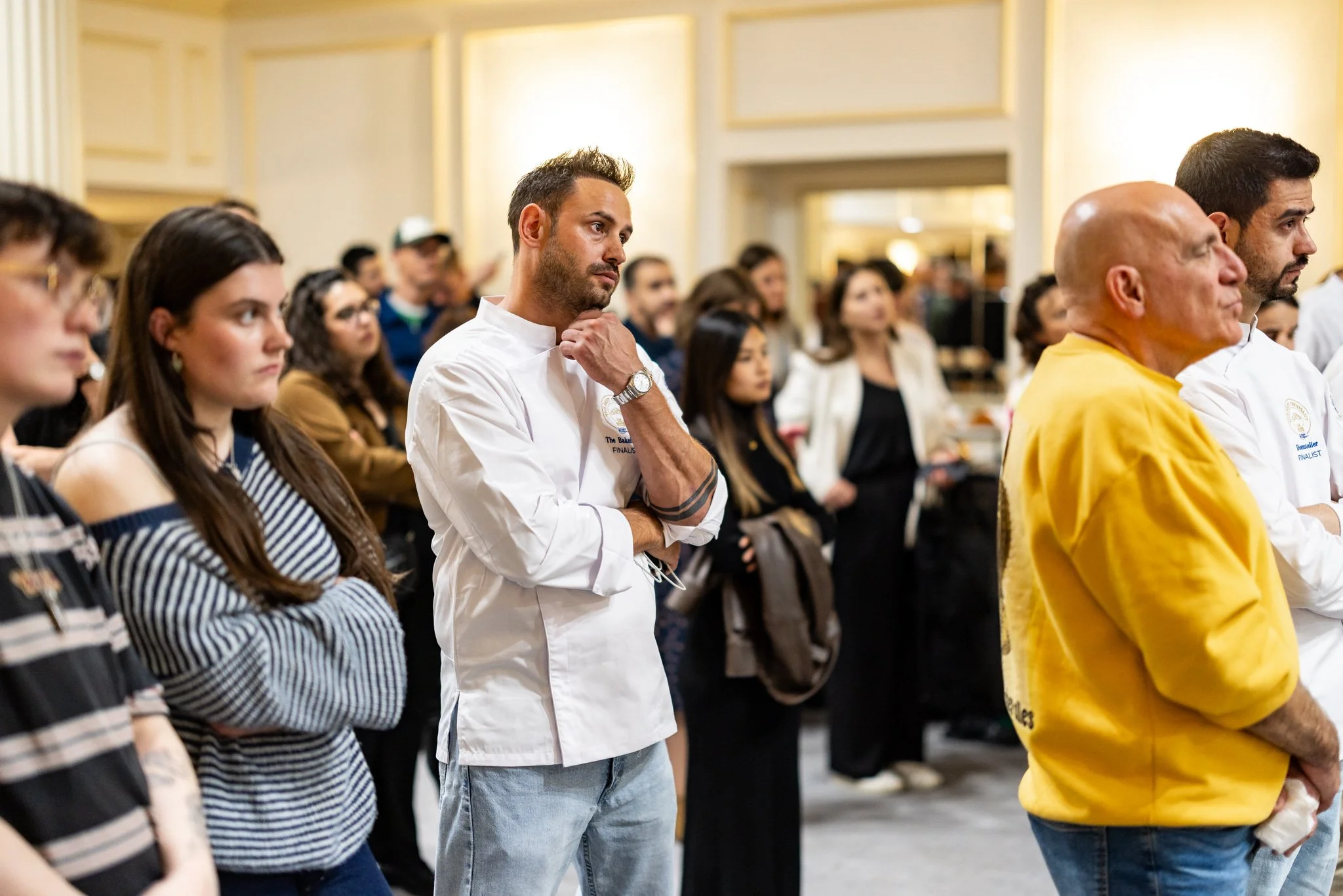 Group of people attending an indoor event, standing attentively in a well-lit room, dressed casually and professionally.