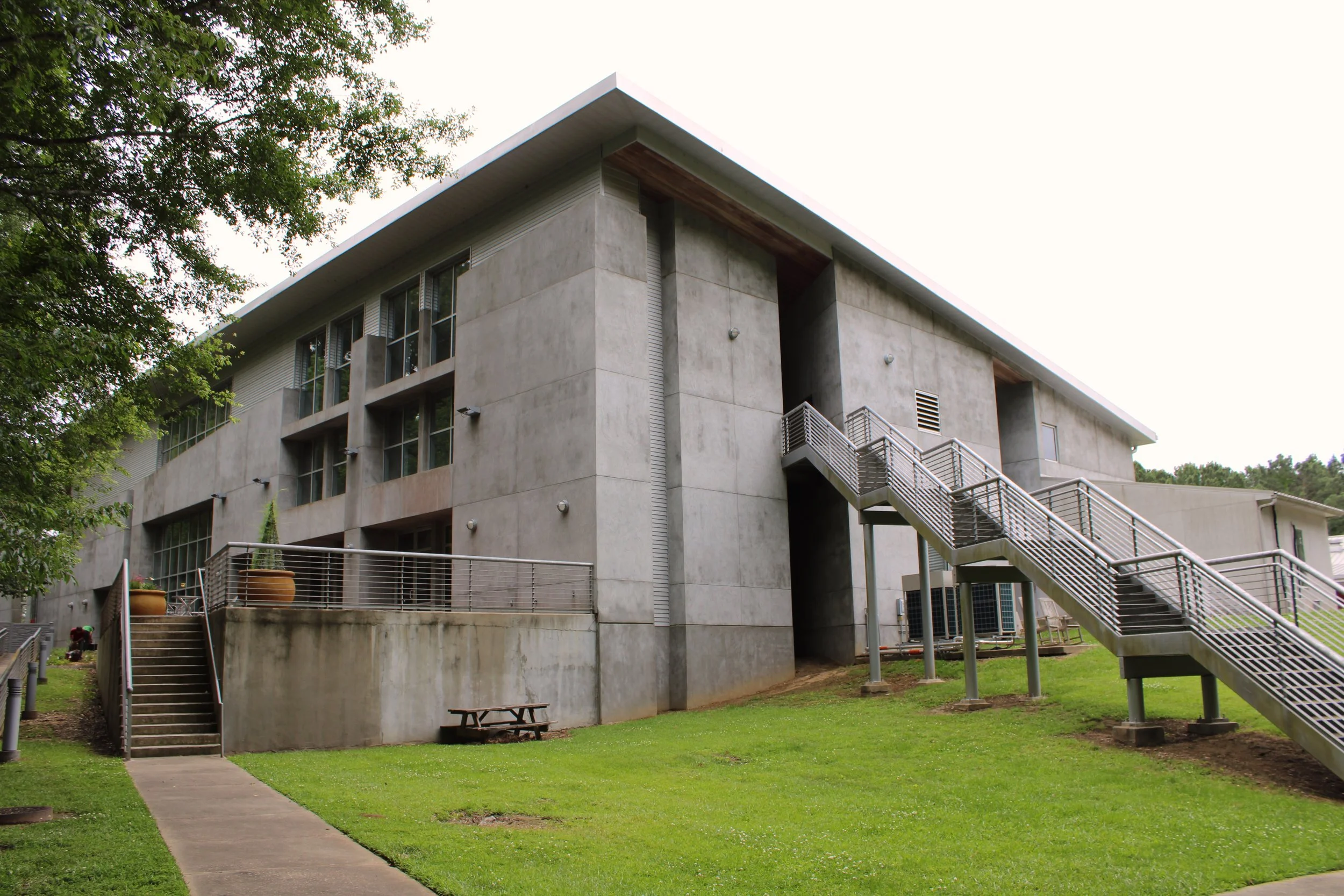 A modern, multi-story concrete apartment building with exterior staircases, surrounded by green grass and trees.