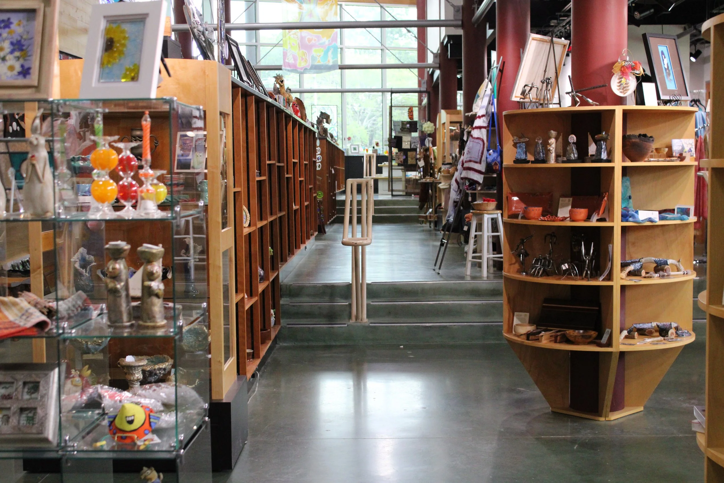 Interior of a store with wooden shelves and display cases containing various decorative items and crafts, with large windows in the background.