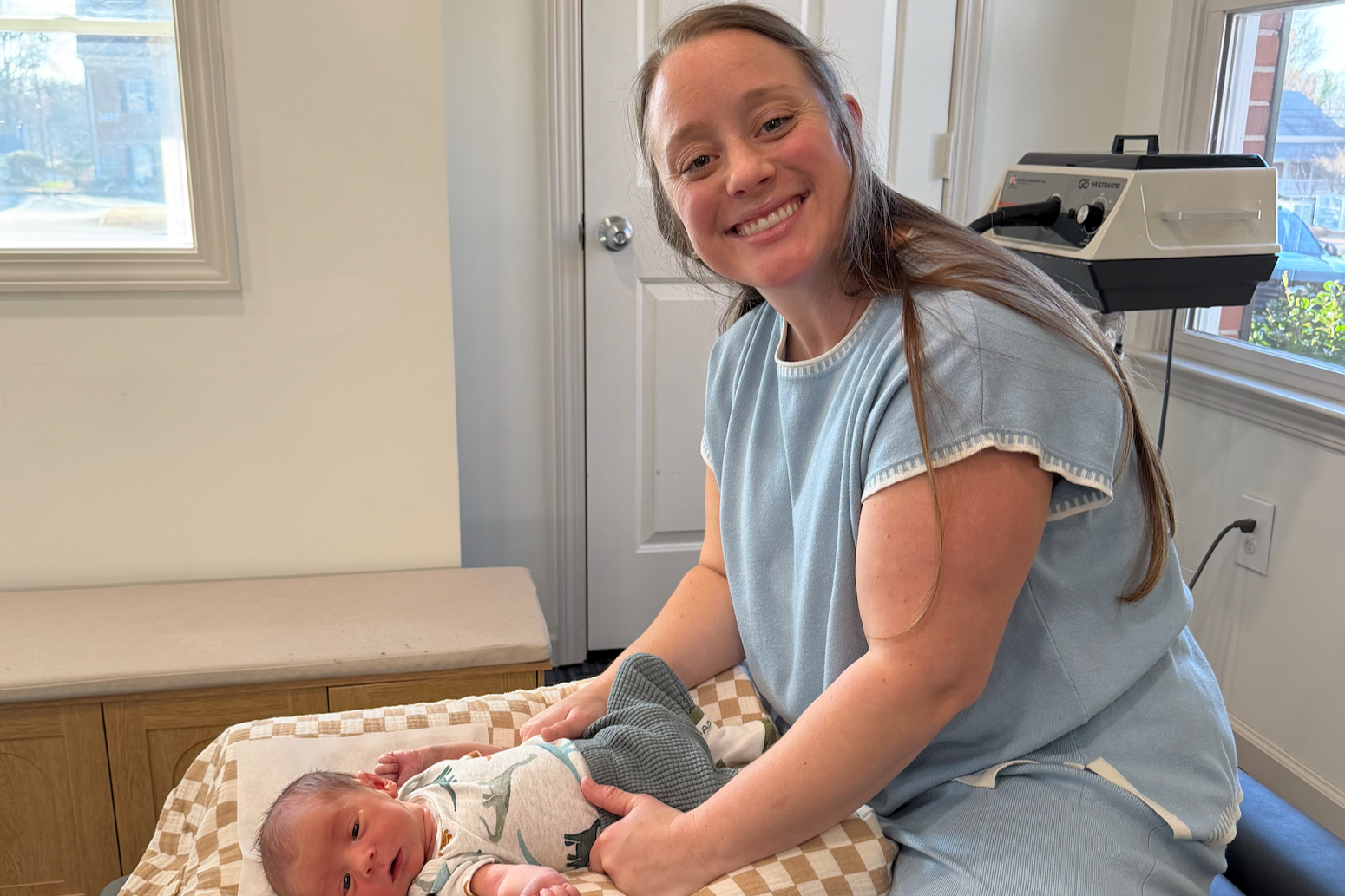 Dr. Mariah smiling while gently adjusting a newborn baby on a checkered blanket on an examination table at Krantz Chiropractic Clinic.