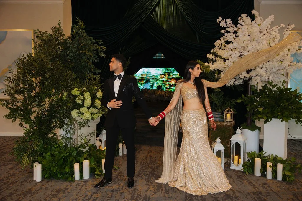 A bride and groom holding hands at their wedding reception, surrounded by floral decorations and lanterns.