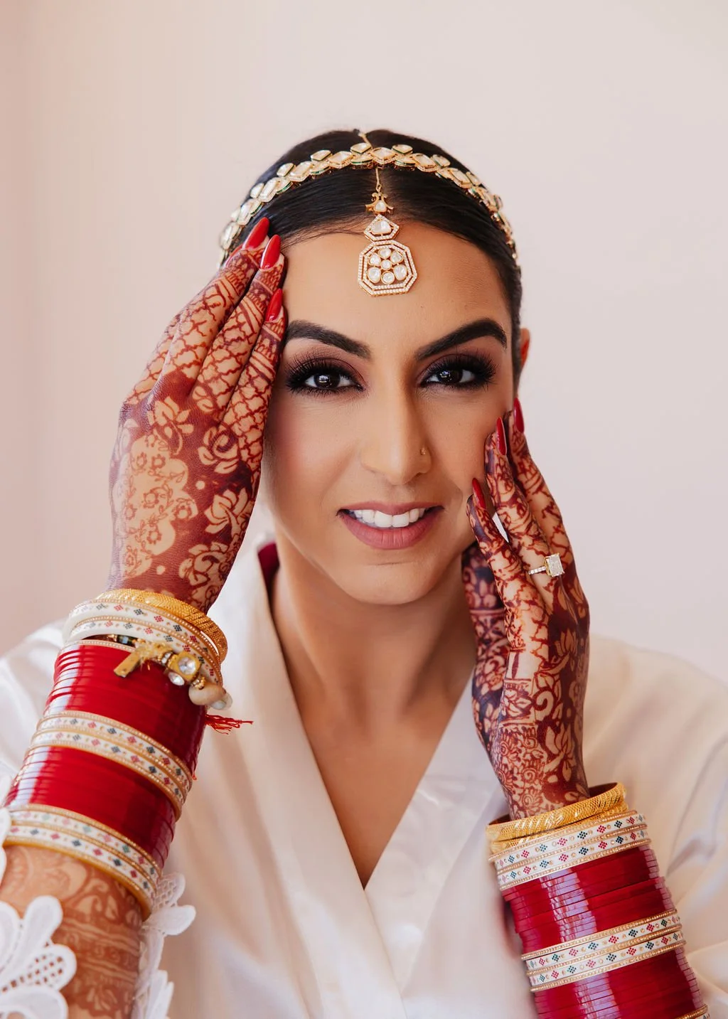 Close-up of a bride getting ready with henna-adorned hands, wearing traditional jewelry and red bangles, smiling at the camera in Hilton Santa Barbara beachfront.