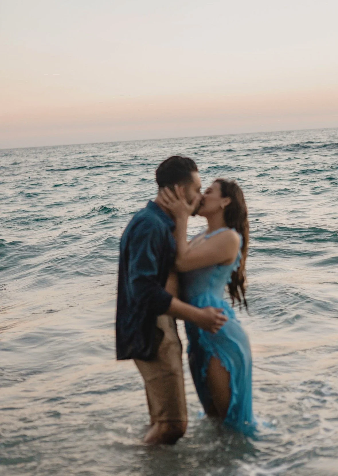 A couple kissing in the ocean at sunset.
