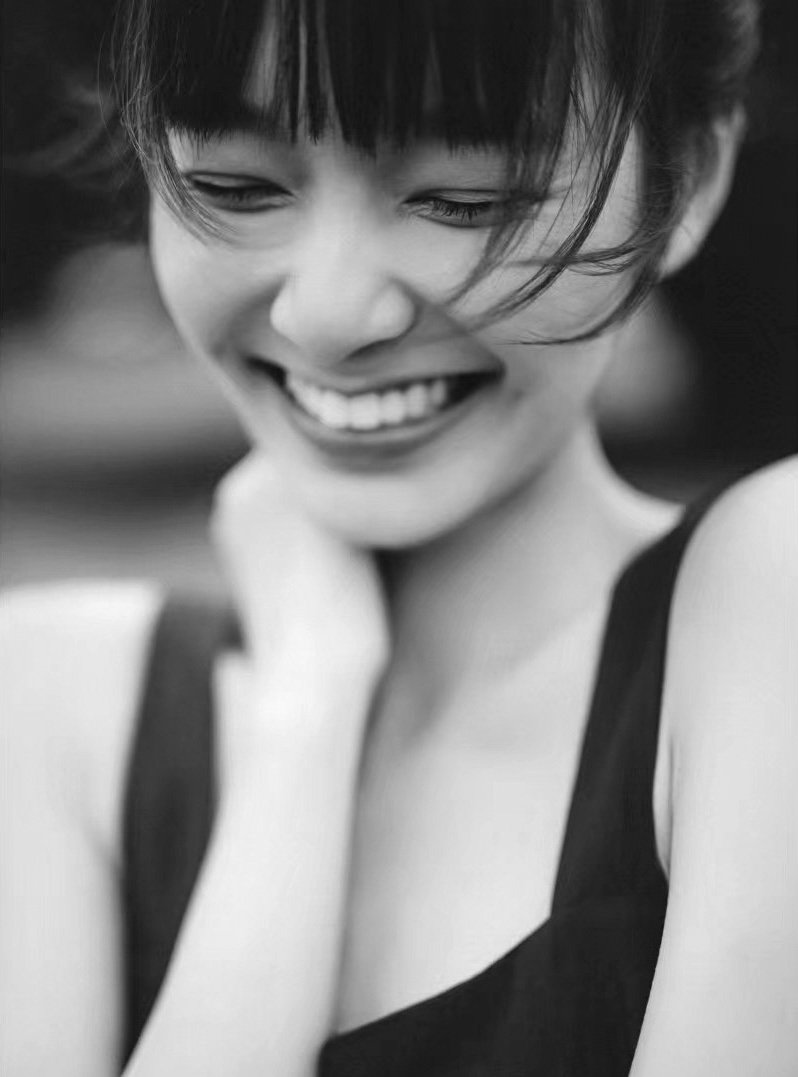 A black and white photo of a young woman laughing with her eyes closed, resting her head on her hand.