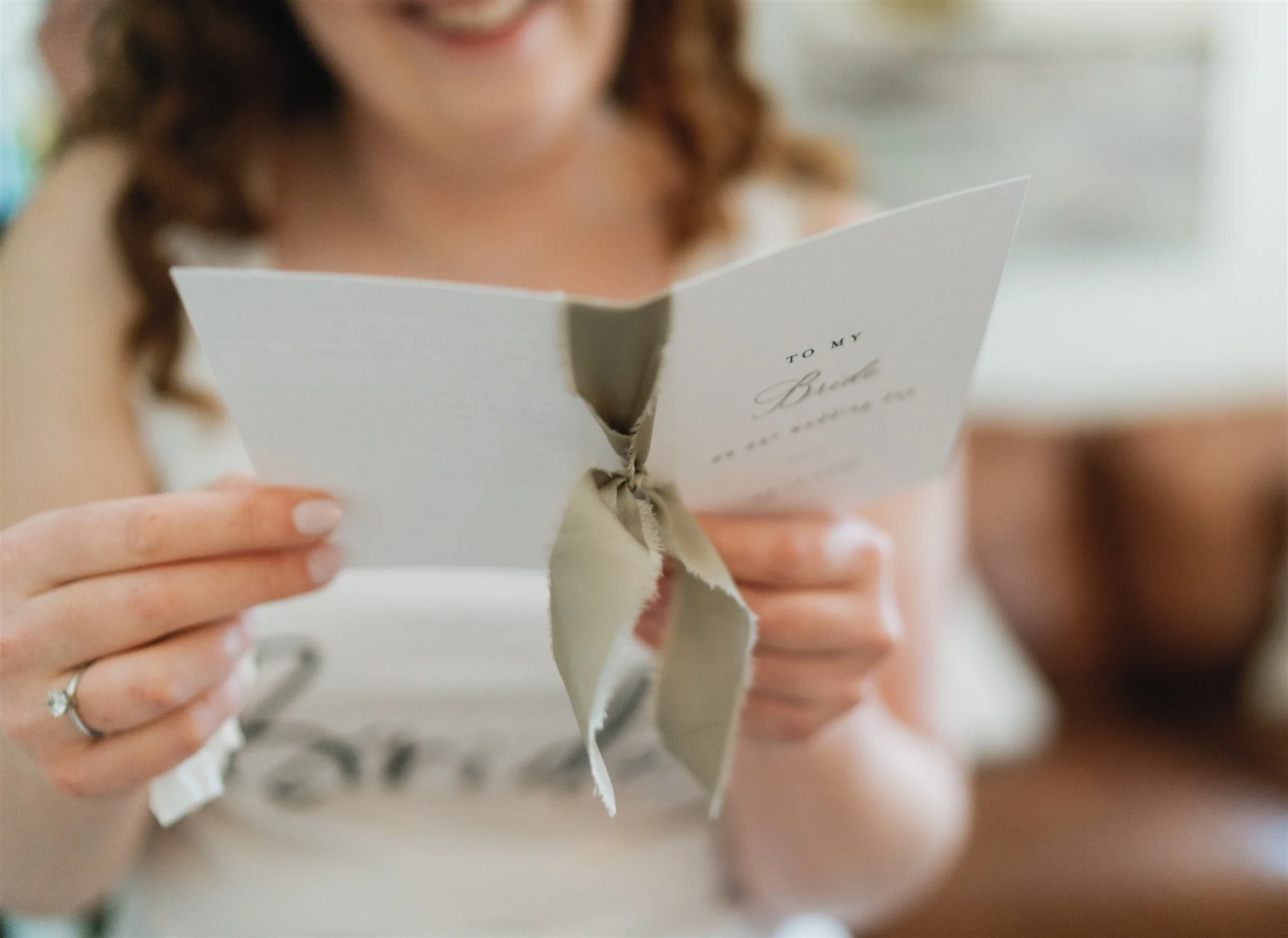 Bride and groom holding hands and smiling, bride in lace wedding dress and groom in gray suit, standing indoors.