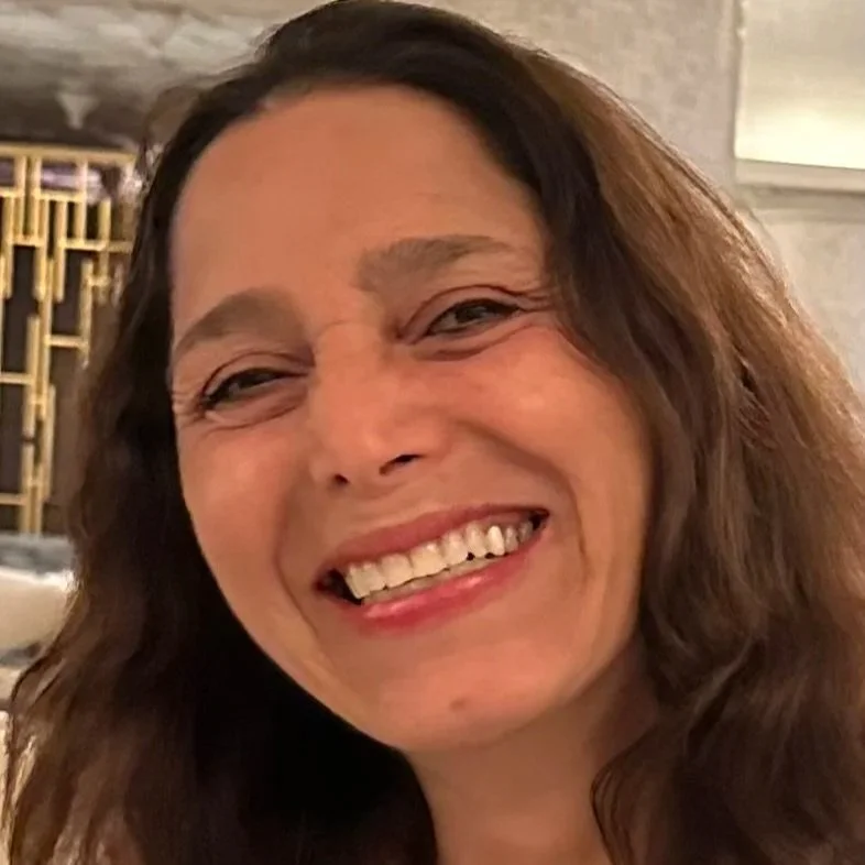 Close-up of a woman smiling in a warmly lit indoor setting with a blurred, modern interior background.